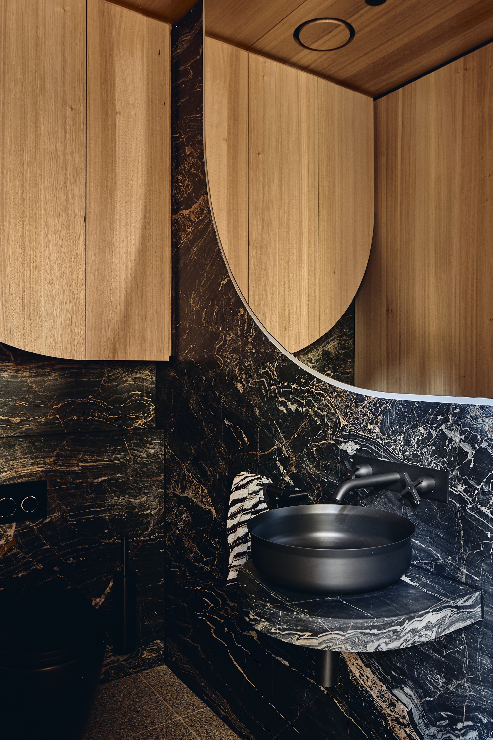 Powder room with dark gold-veined stone walls, a black basin on a curved stone shelf and arched timber cabinet doors above