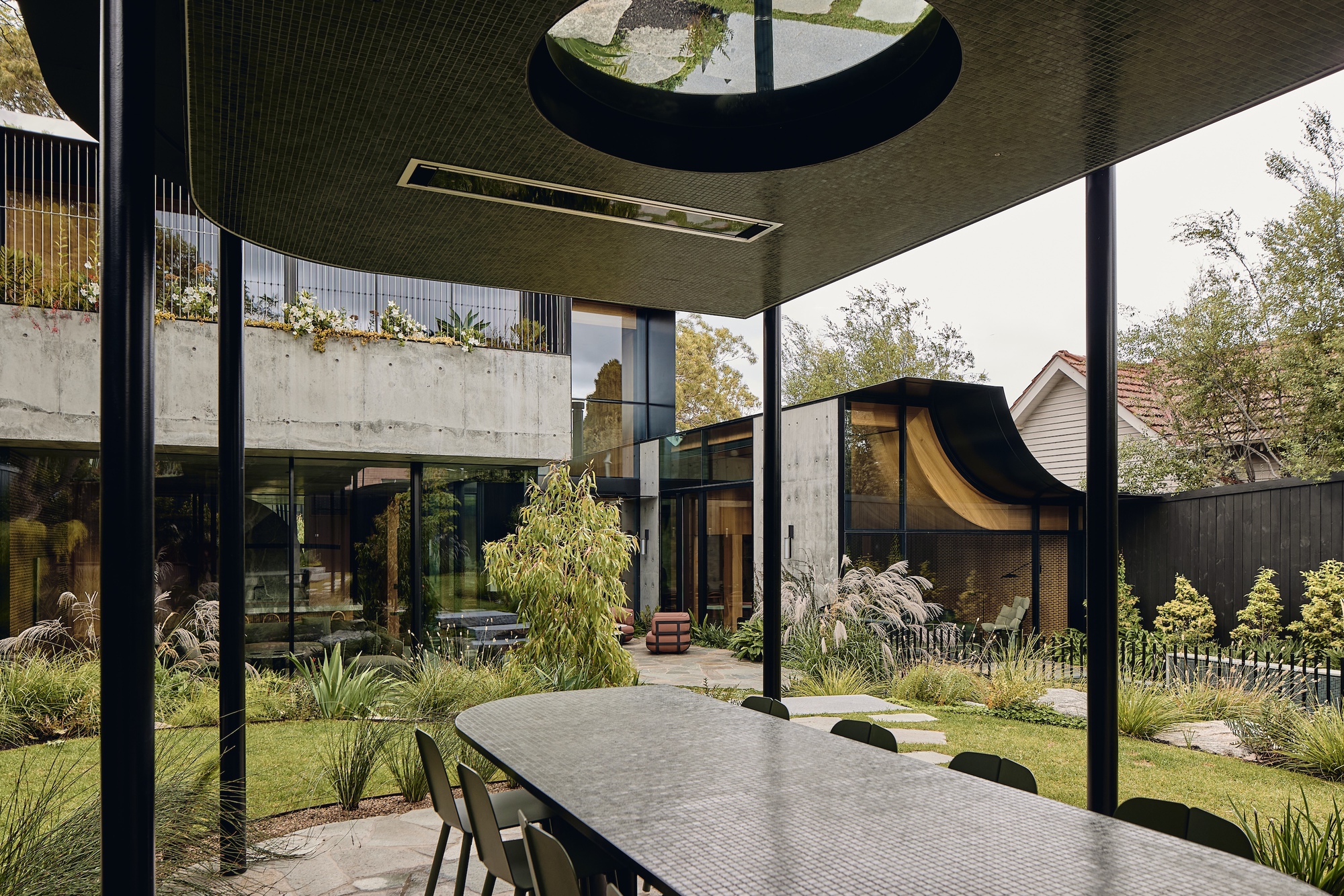 View from under a mosaic-clad canopy with oval skylight, over a long table toward the garden and glazed rear wing
