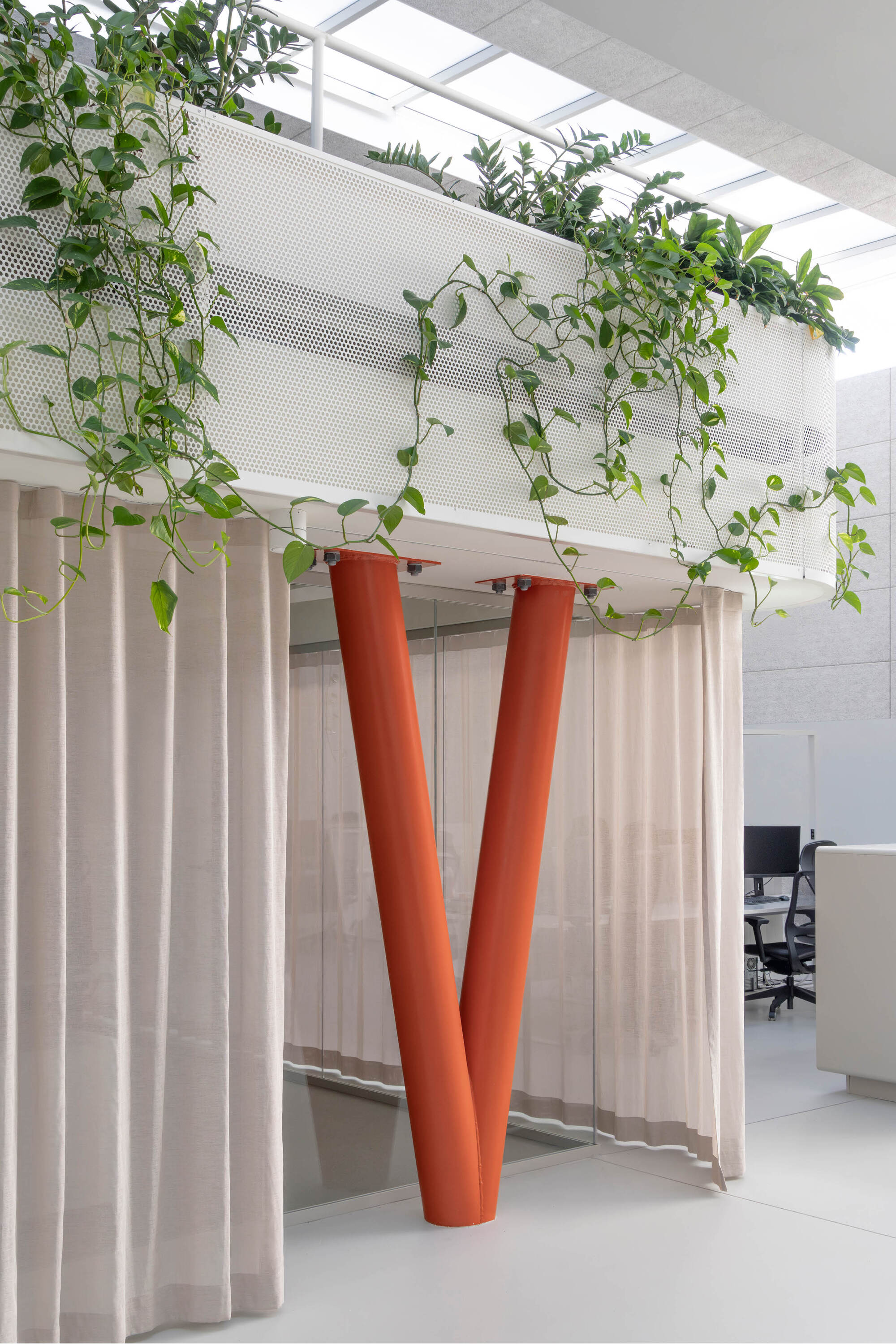 V-shaped orange column rising beside sheer curtains below a perforated metal planter with pothos trailing down