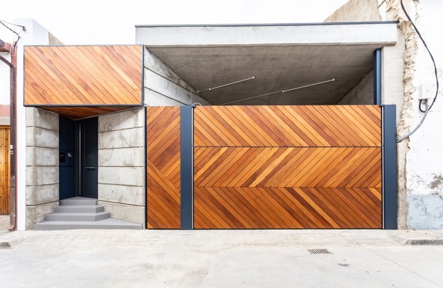 Street facade with diagonal timber slat garage gate and entry canopy beside board-marked concrete walls and a small stepped threshold