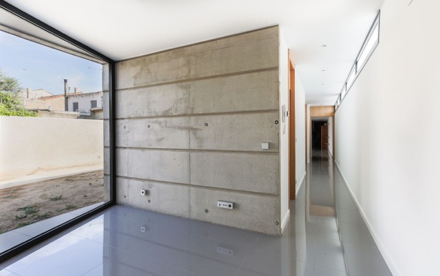 Corridor corner with board-marked concrete wall, floor-to-ceiling corner glazing and a clerestory strip over glossy grey floor