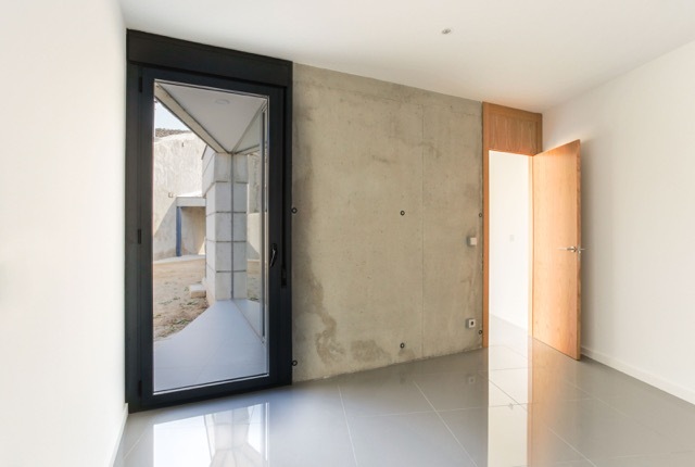 Bedroom interior with a black-framed glass door opening to the courtyard, a bare concrete wall and an open oak door