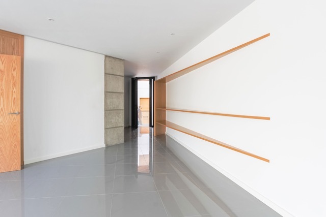 Corridor with recessed timber shelves in a white wall, a concrete column and polished grey floor leading to a dark doorway