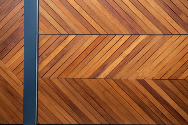 Close-up of the herringbone timber gate cladding in warm brown tones, divided by a vertical dark steel post
