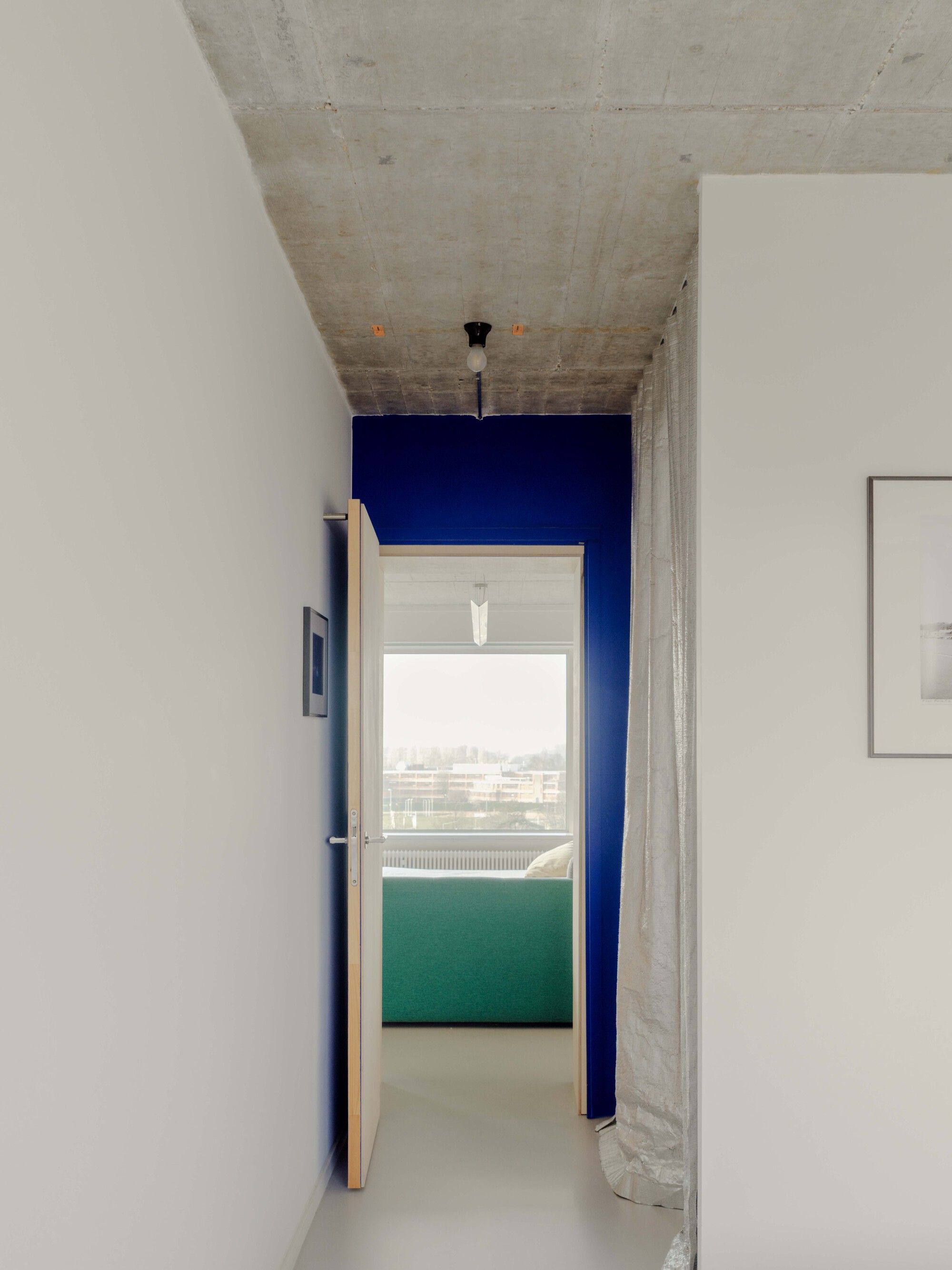 Corridor with a cobalt blue end wall, open timber door and green sofa glimpsed against a bright window