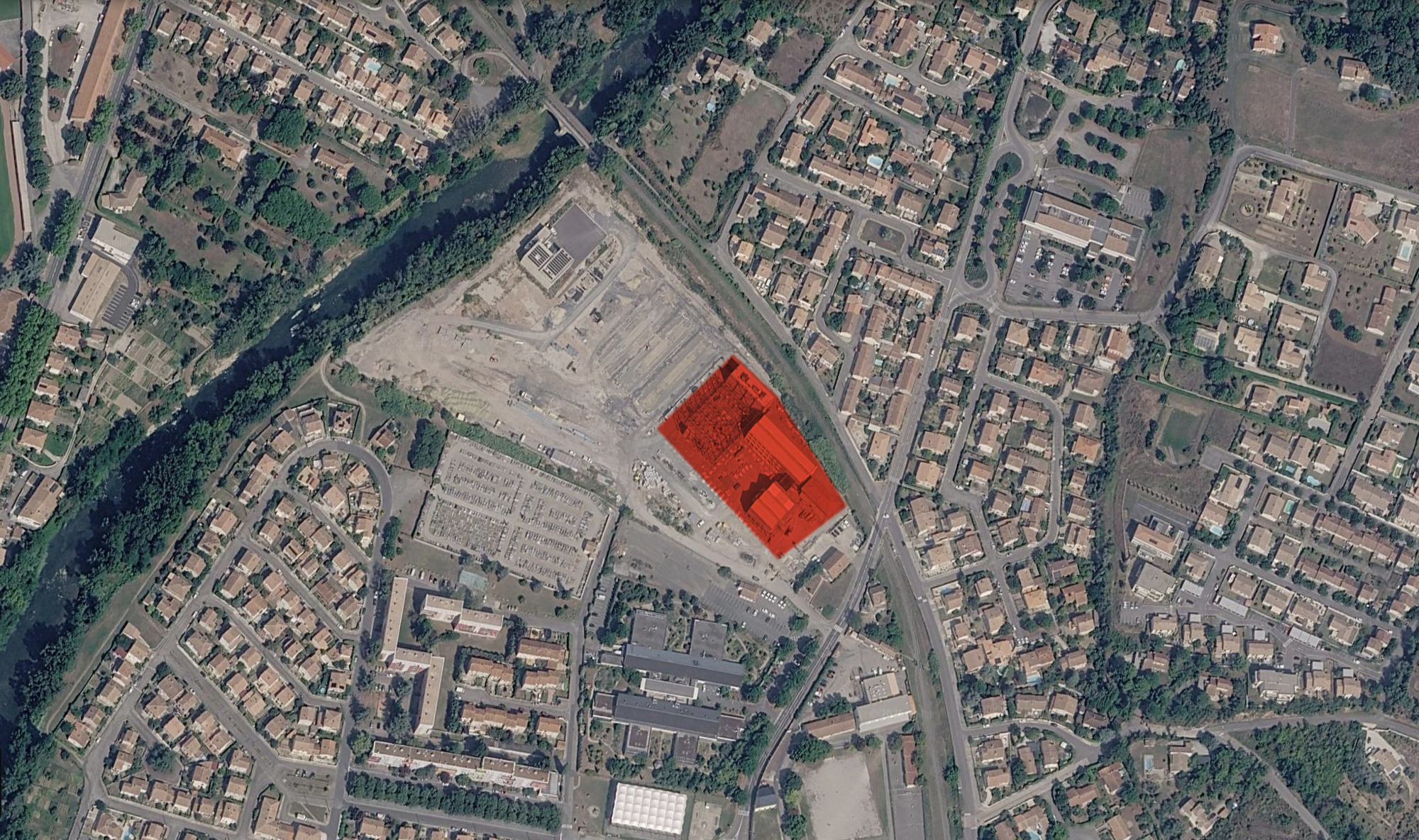Aerial site plan photograph with the building footprint highlighted in red among housing, a river and a cleared lot