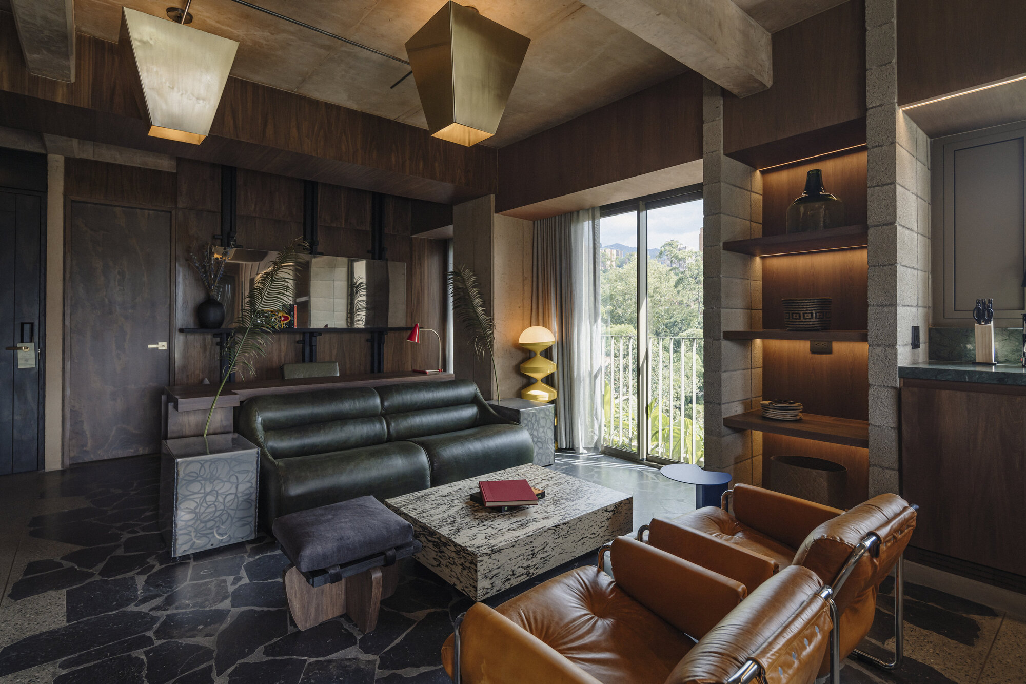 Living room with green leather sofa, tan leather armchairs, stone coffee table and shelves lit beneath a timber-clad wall