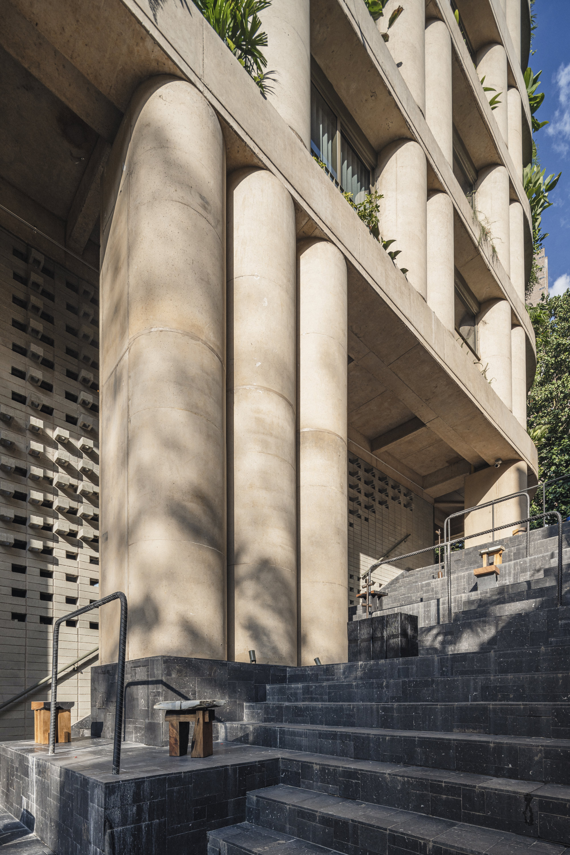 Base of the tower with rounded concrete columns above dark stone steps, dappled in afternoon sunlight and shade