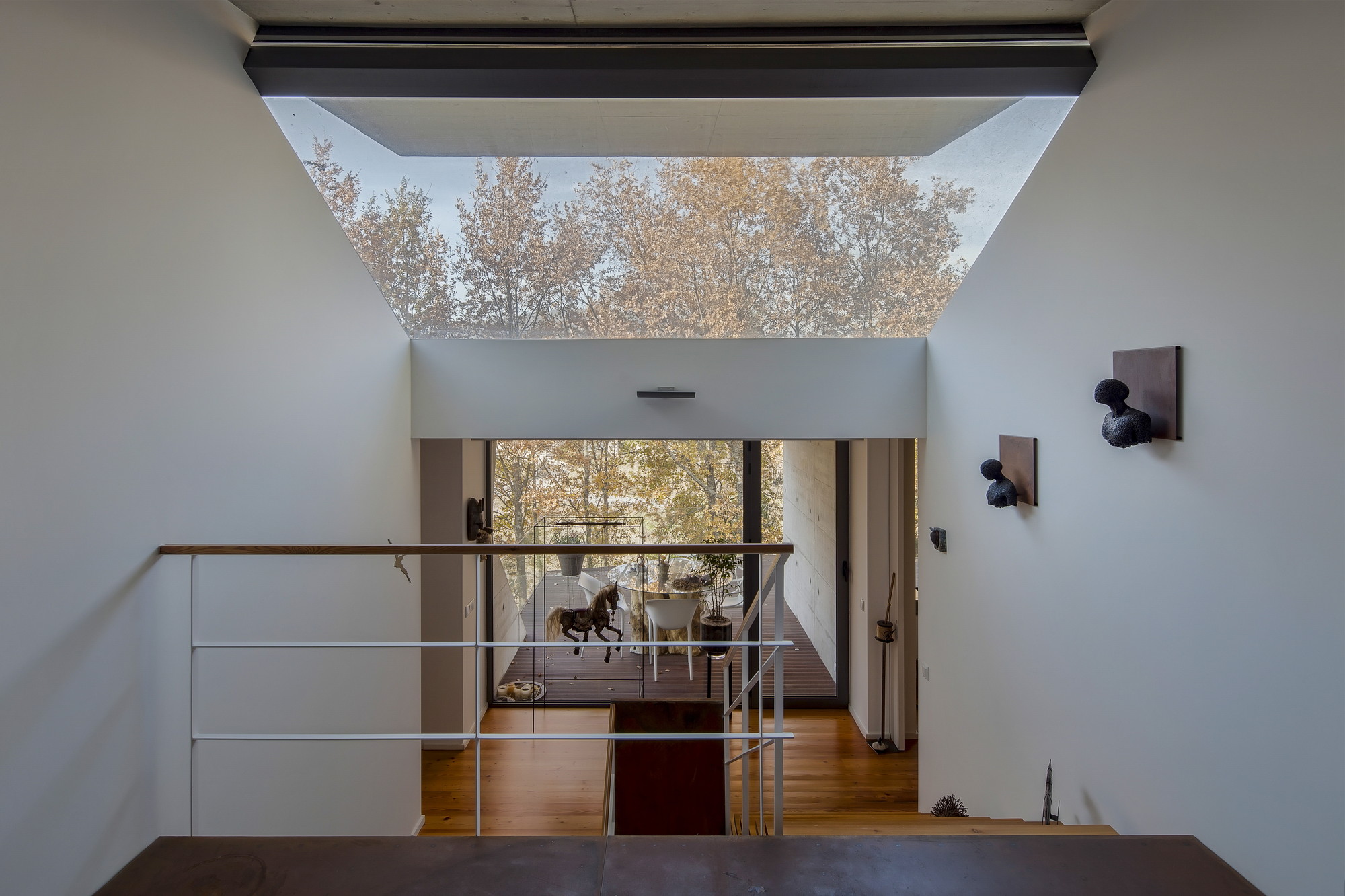 Stair landing with white walls and a skylight framing autumn treetops, with a wooden floor and terrace seen beyond the railing