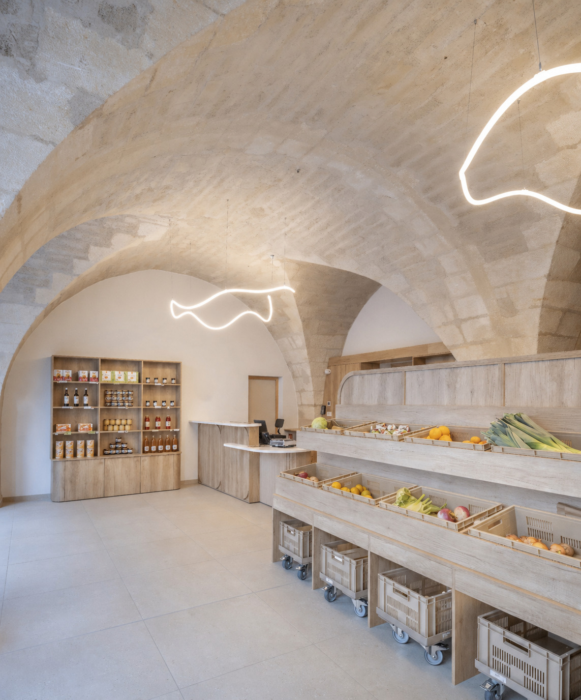 Shop interior with stone groin vaults, timber produce shelving on wheeled crates and looping light fixtures hanging overhead