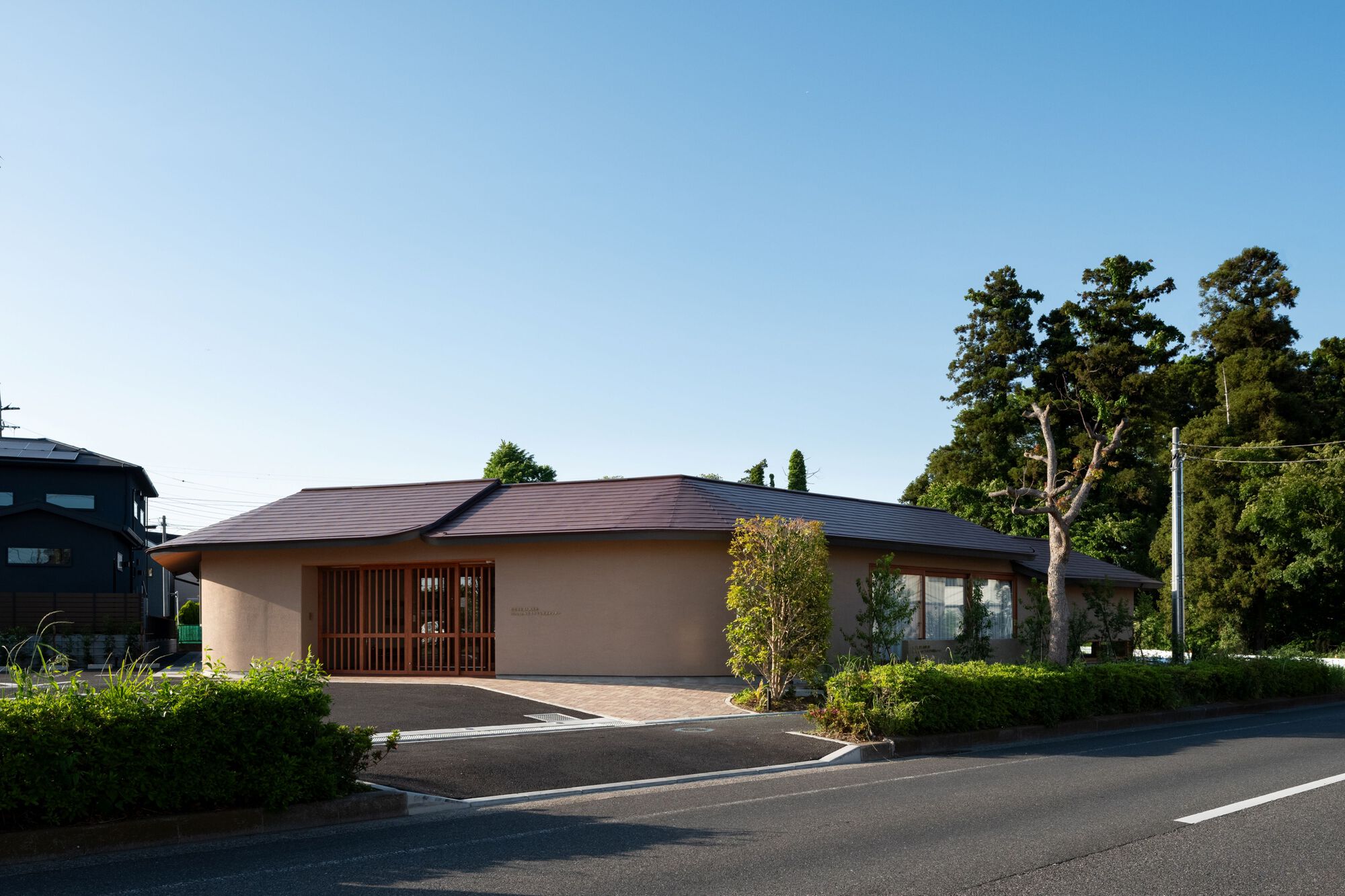 Street view of the low plaster-walled building with a timber lattice entrance screen under a clear blue sky