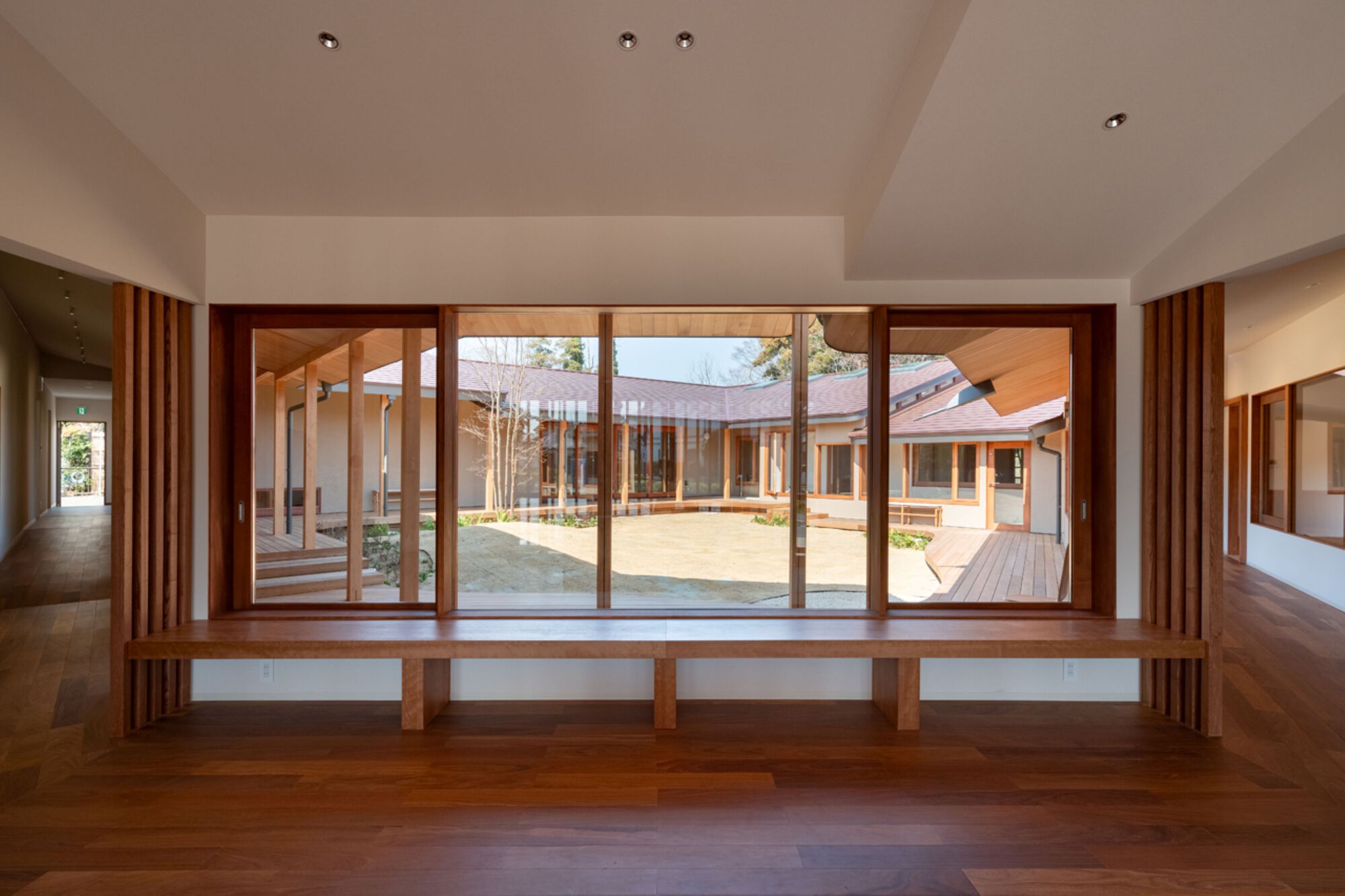 Interior window bench facing the courtyard, framed by vertical timber slats and a walnut floor in clear afternoon light