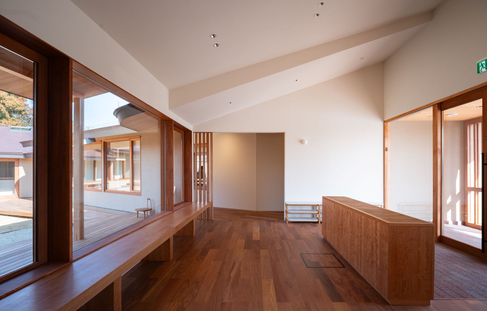 Open room with a long timber window bench, a wooden counter and a sloped white ceiling beside courtyard glazing