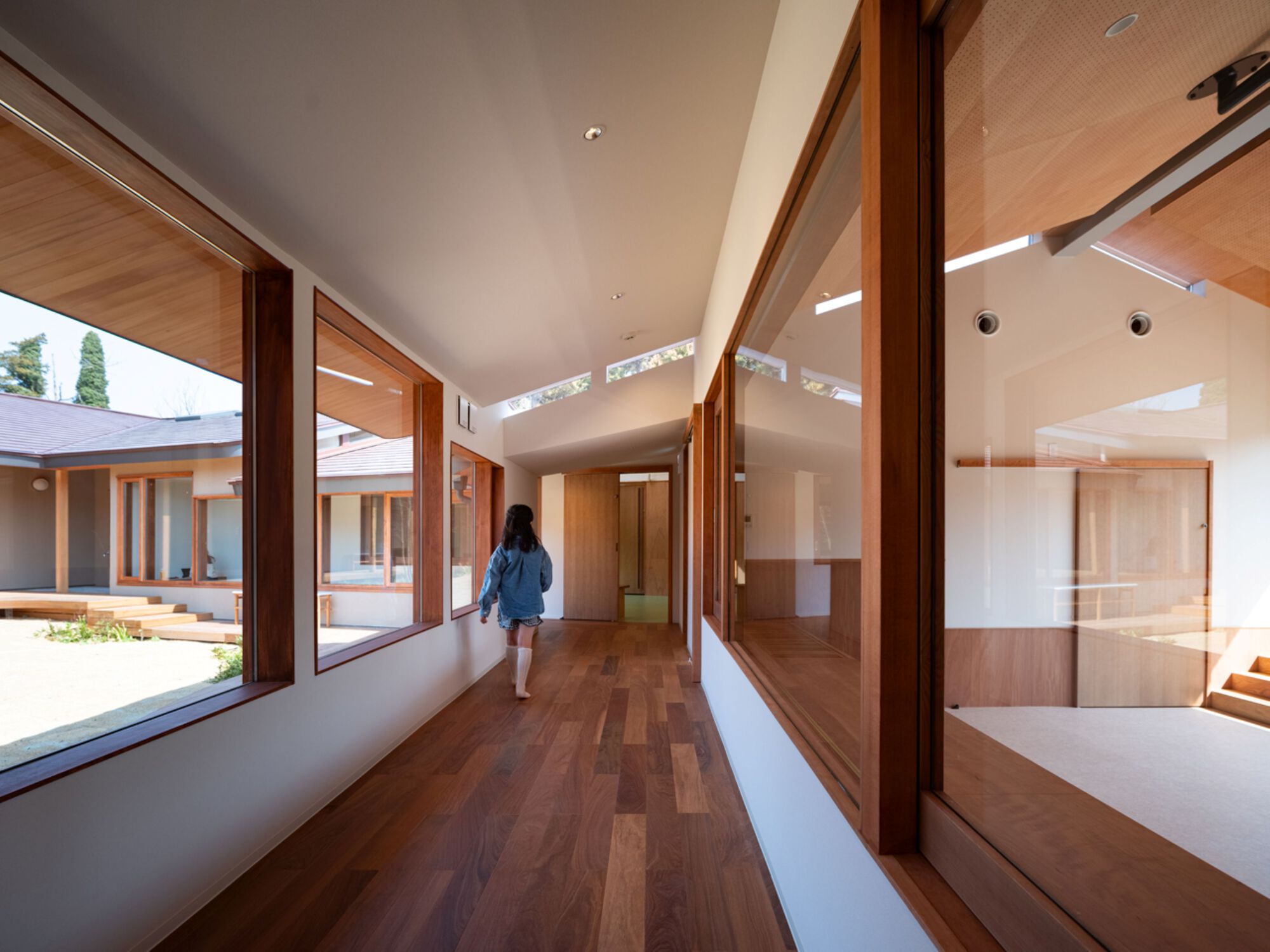 Child walking down a hardwood corridor lined with timber-framed windows that look onto the sunlit courtyard and clerestory glazing