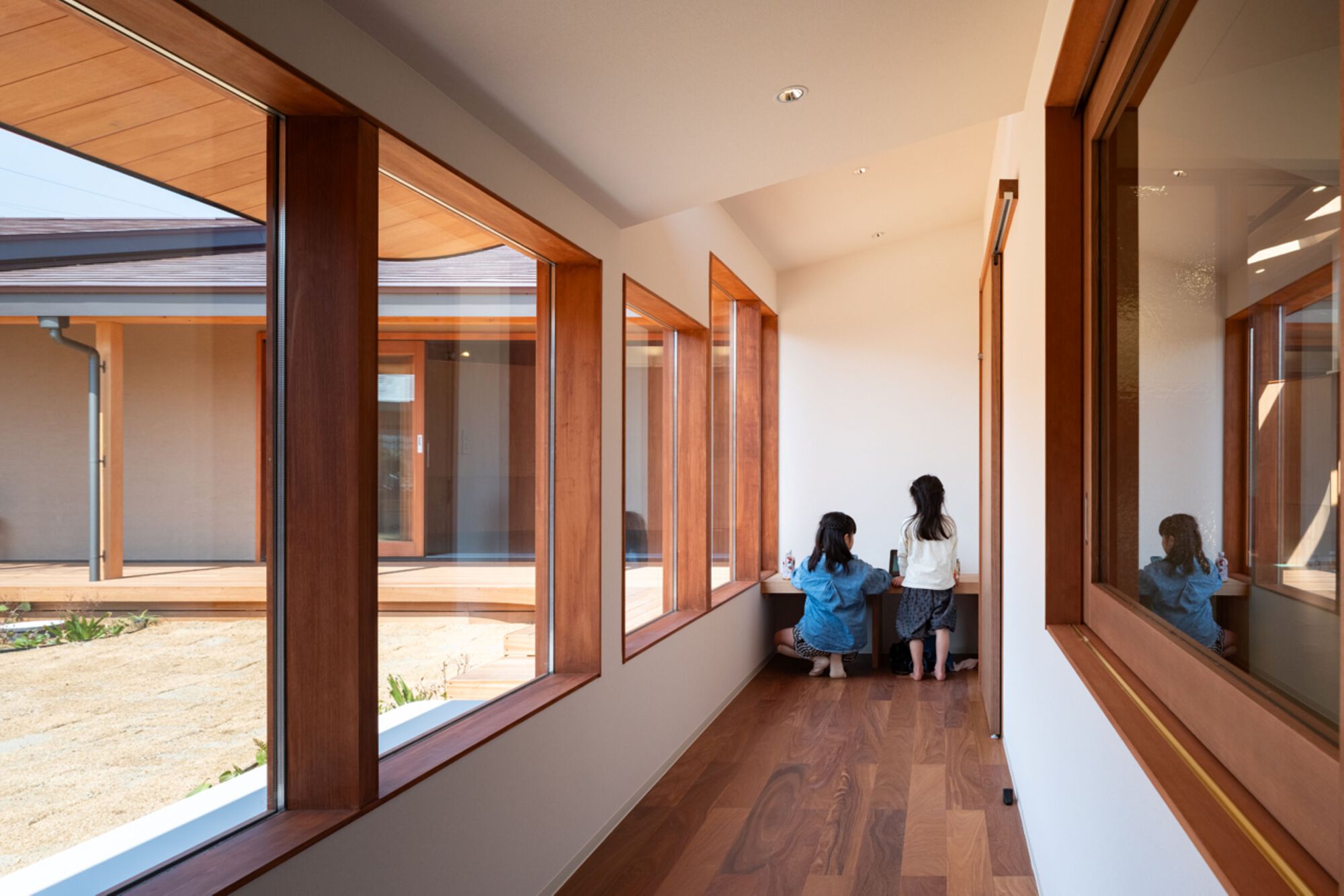 Two children seated at a built-in desk at the end of a narrow corridor with courtyard windows alongside