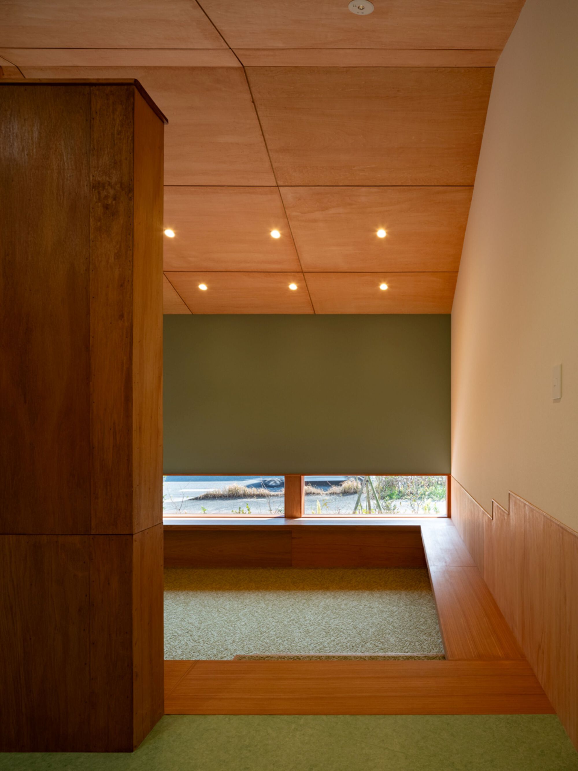 Sunken carpeted nook with a stepped timber edge and a low strip window beneath a green wall and recessed ceiling lights