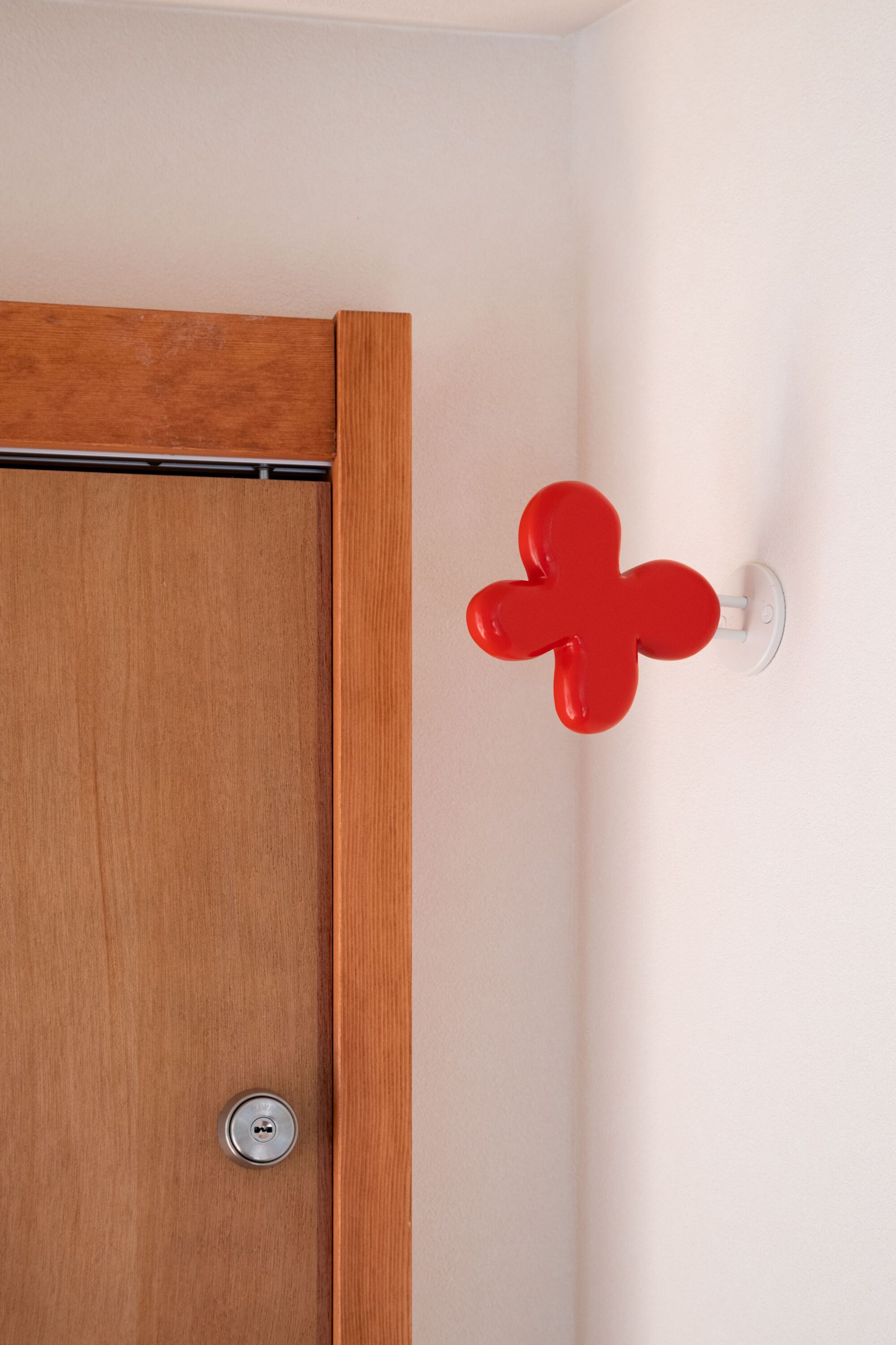 Close-up of a red four-lobed wall hook beside a timber door frame and a steel round door knob