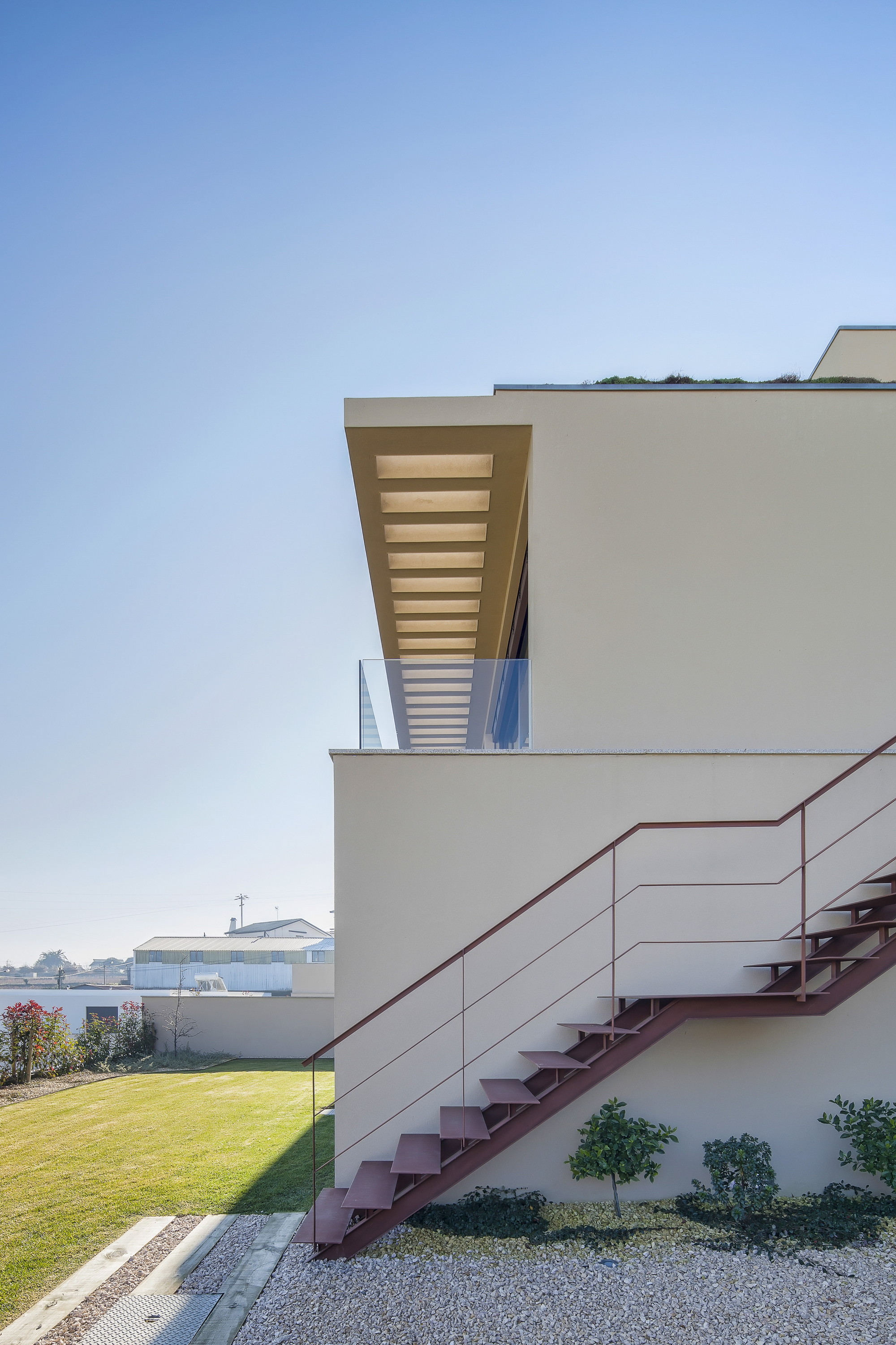 Side elevation of a steel staircase with thin rails rising past a rendered wall to a glass-edged terrace under a timber-lined overhang