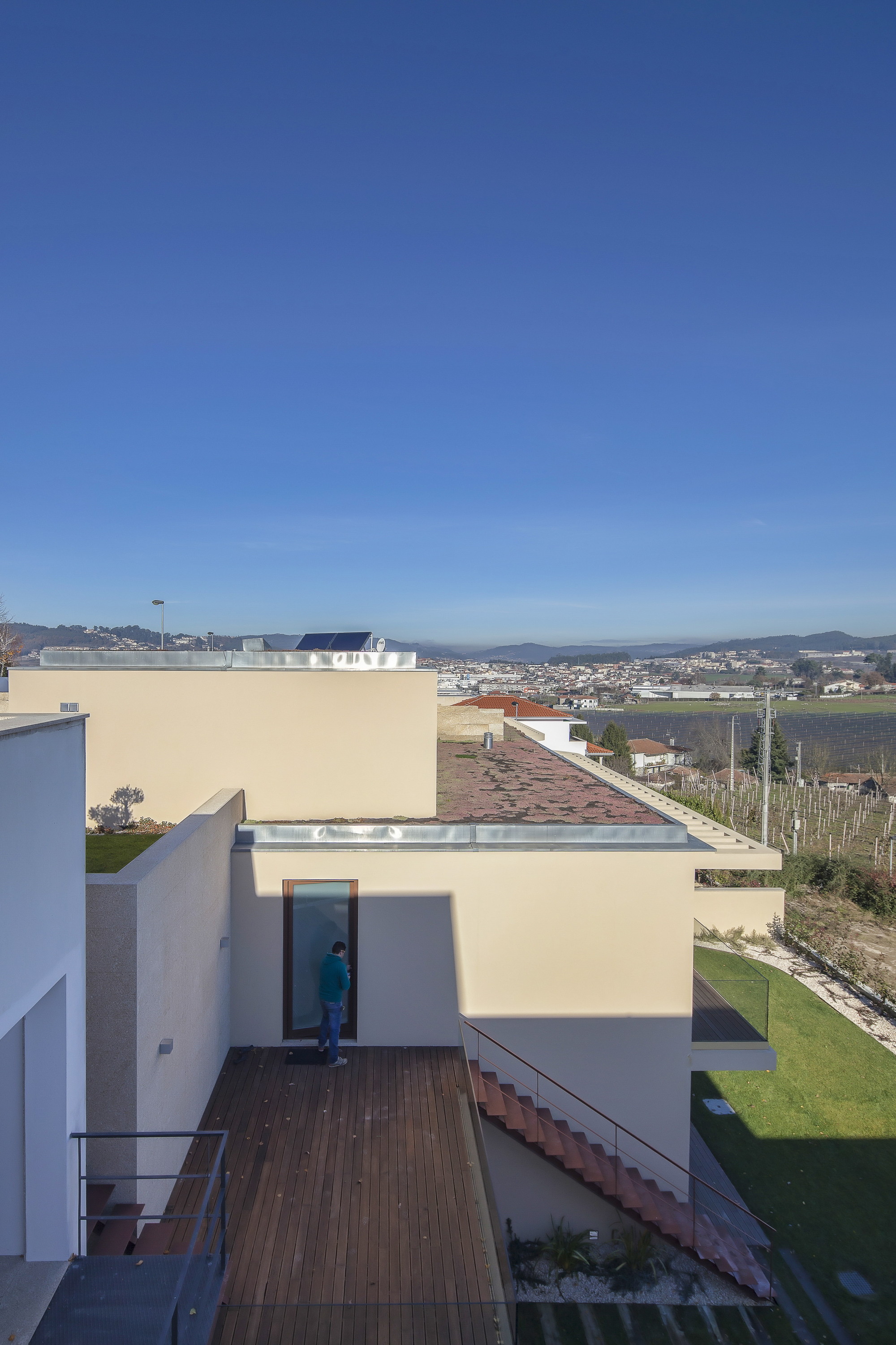 Rooftop and deck level with a person at a glazed door, terracotta steps and vineyards beneath a clear blue sky