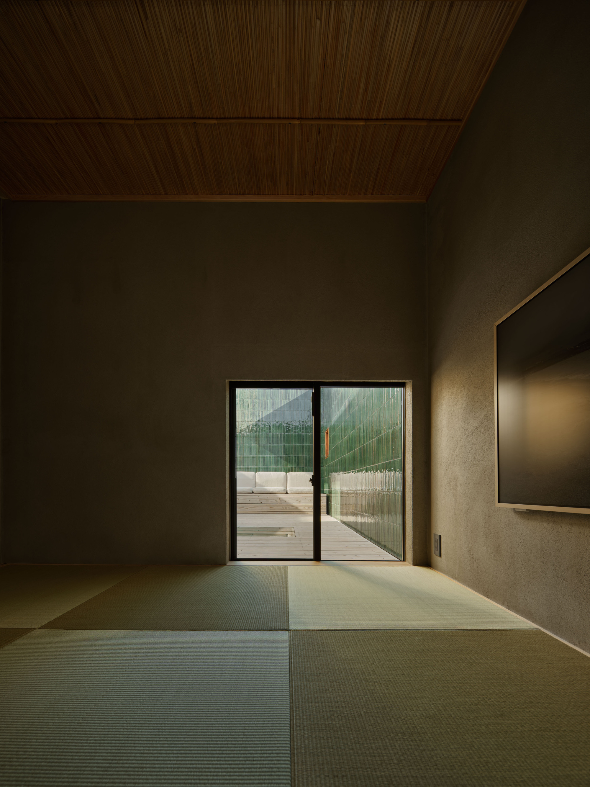 Tatami room with a reed ceiling and sliding glass door framing a green tiled courtyard wall in low light