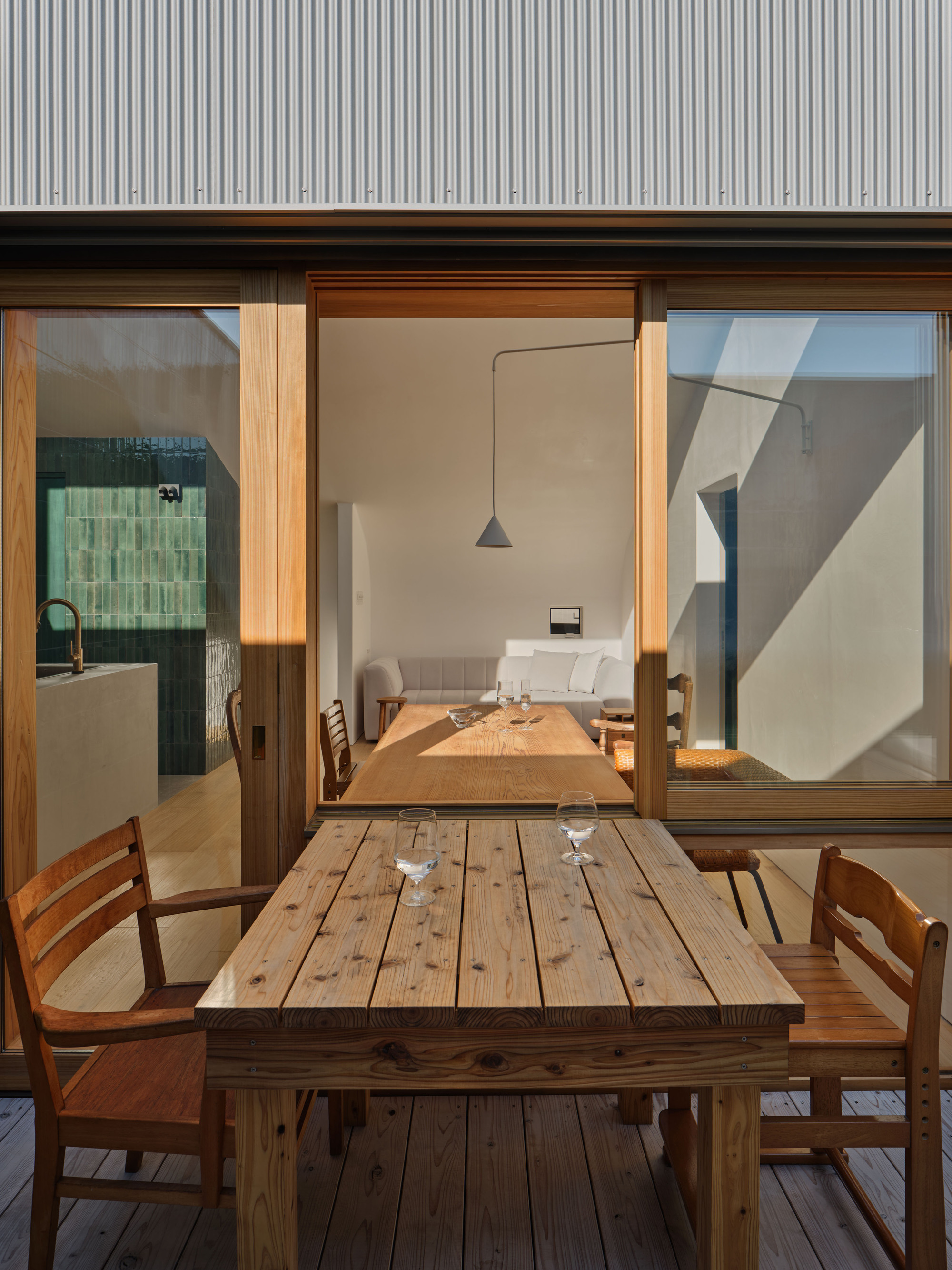 Timber dining table with wine glasses on the deck, set before sliding glass doors and a corrugated metal facade