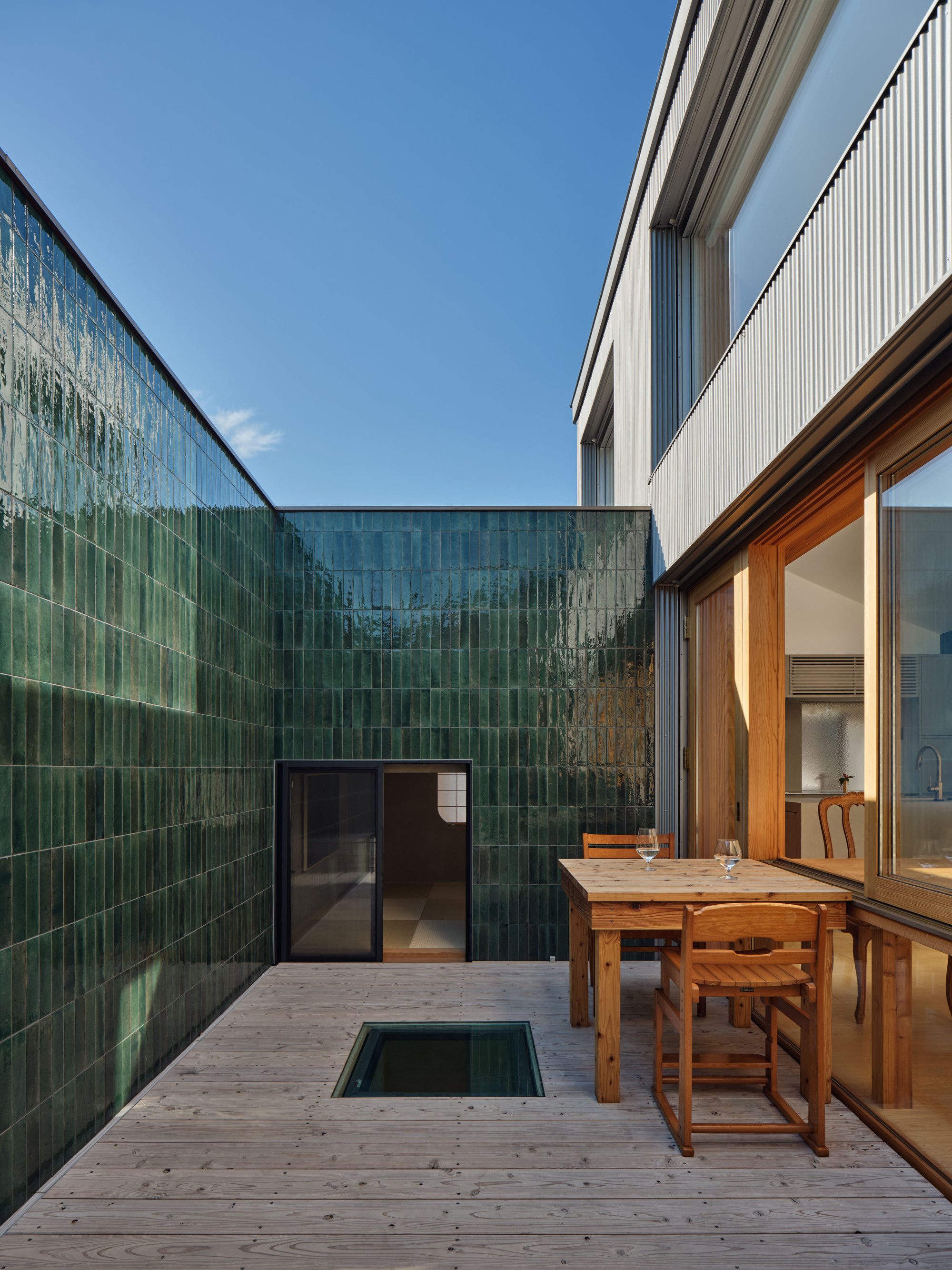 Courtyard deck enclosed by glossy green tile walls, with a floor skylight and wooden table under a clear blue sky