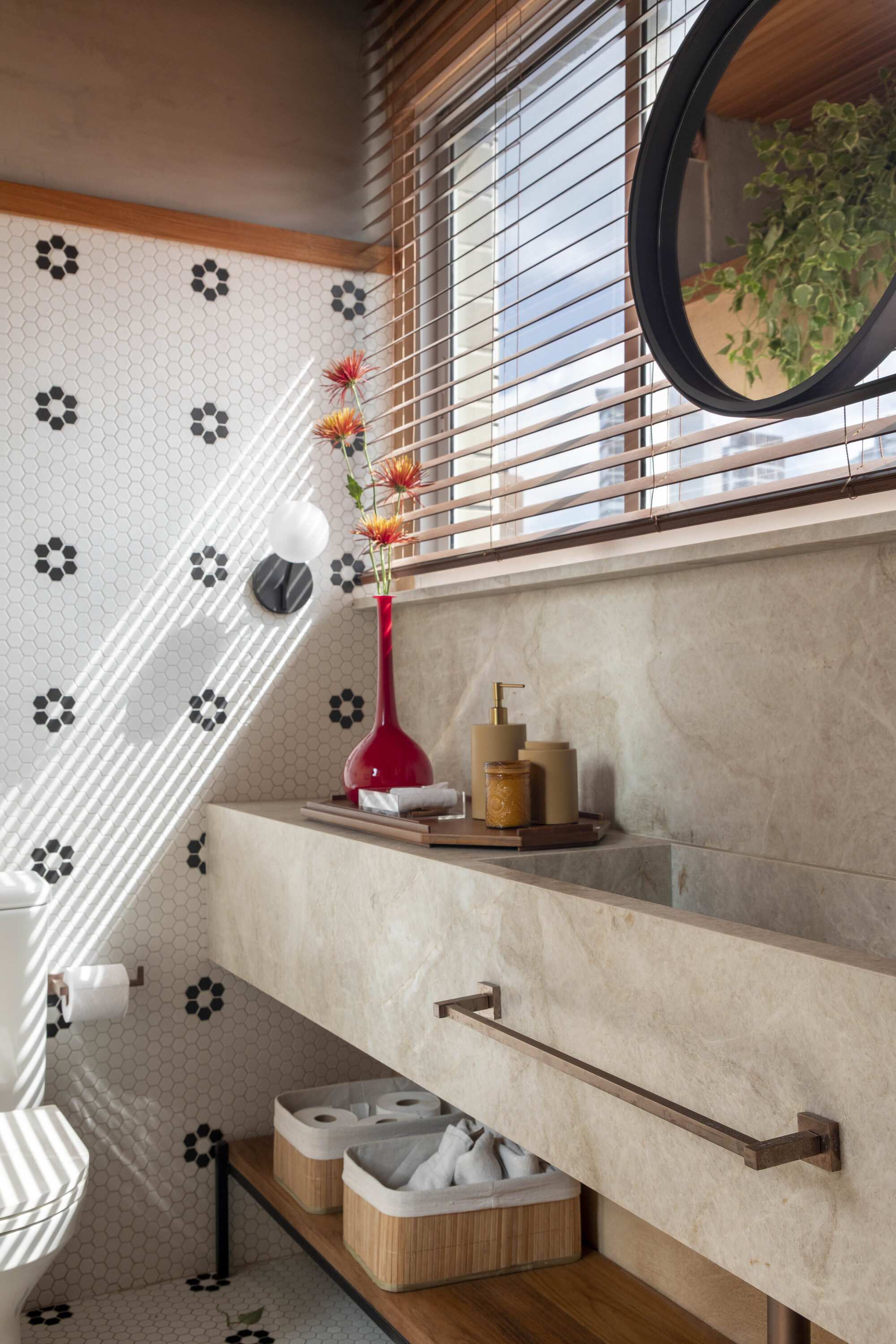 Bathroom with a stone wall-hung basin, hexagonal flower-pattern tile and a red vase in striped afternoon sunlight