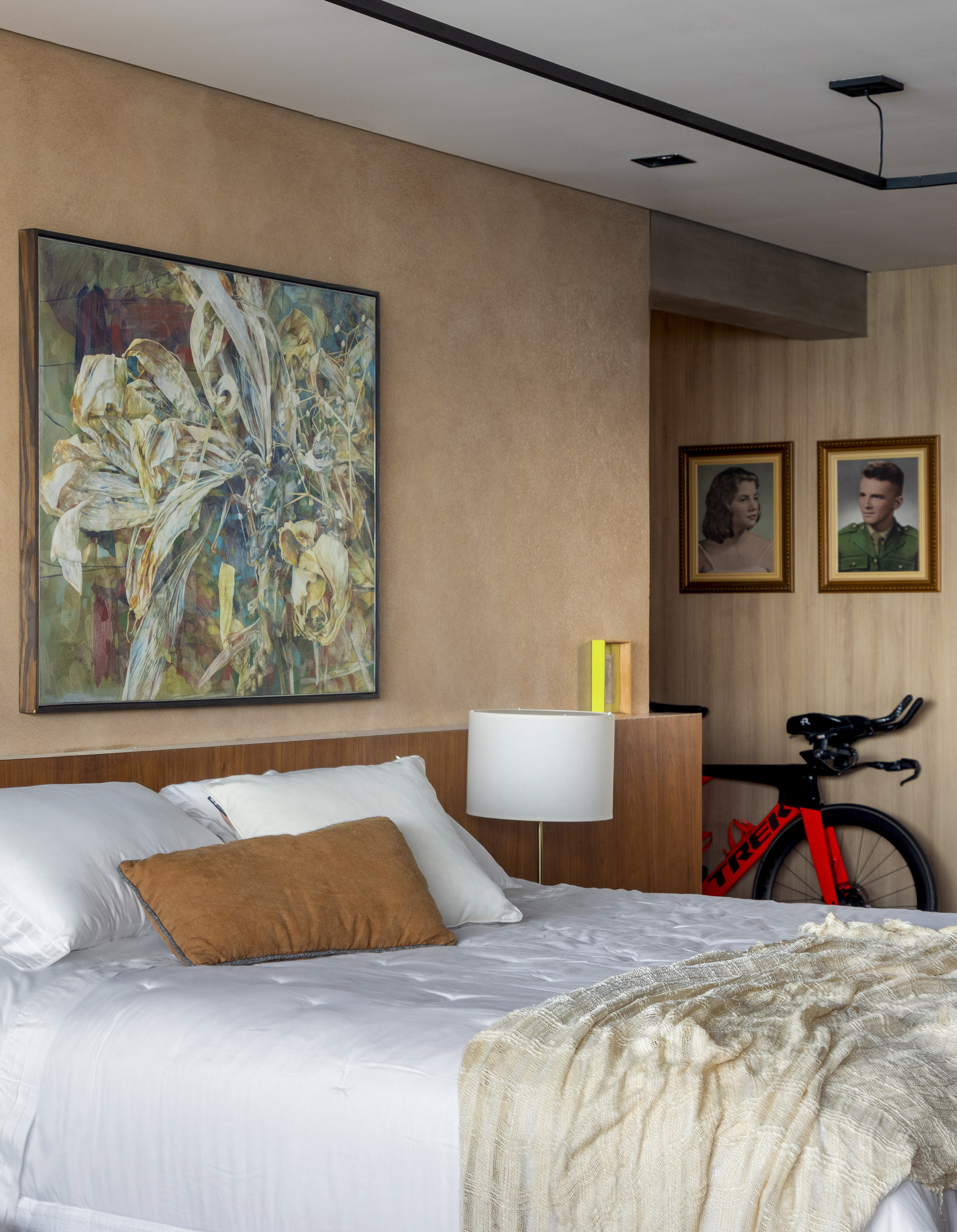 Bed with white linens and a tan cushion beneath a large floral painting, a red triathlon bike in the corner