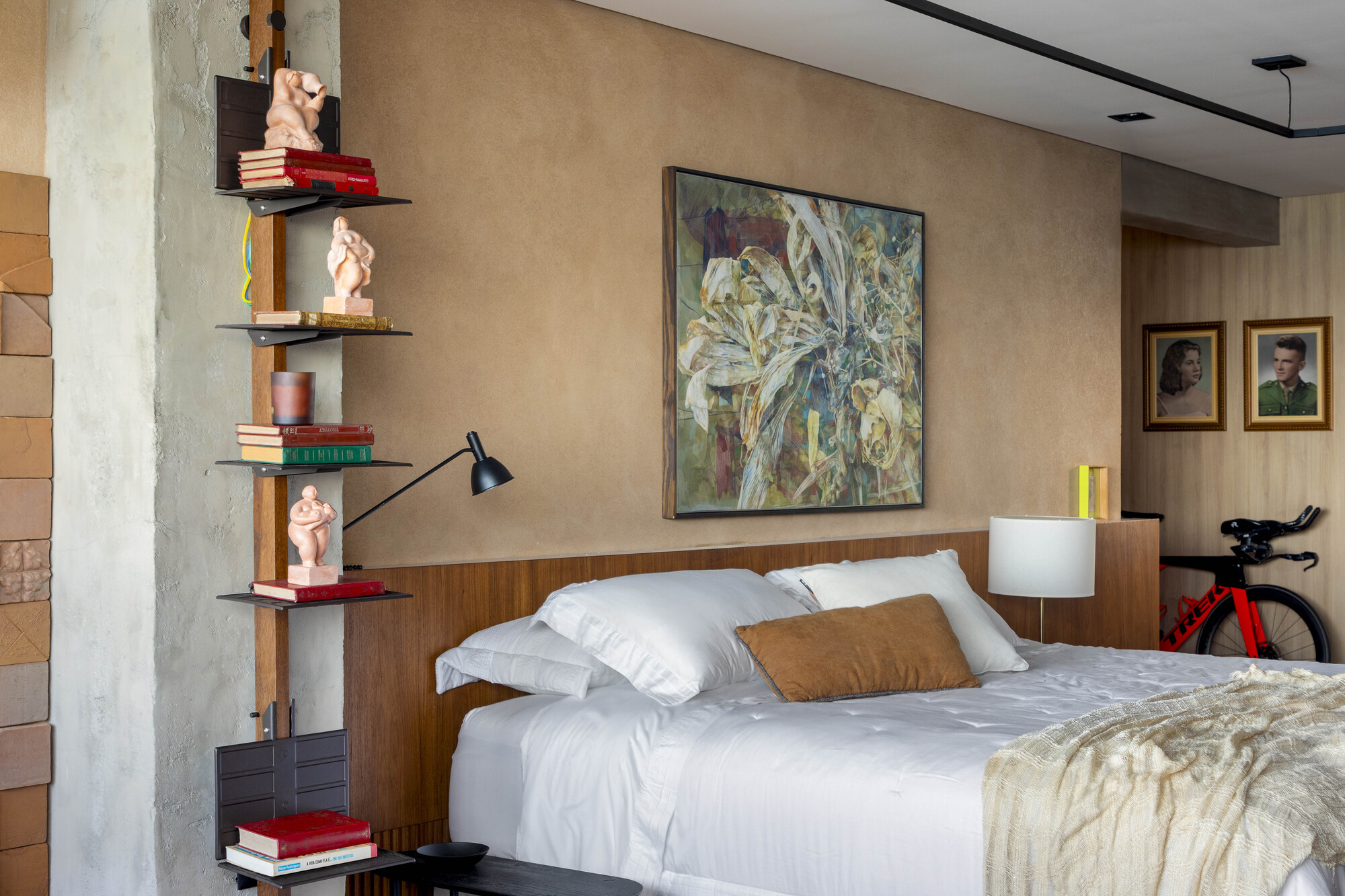 Bedroom wider view with a steel shelf of red books and figurines on a concrete column beside the bed
