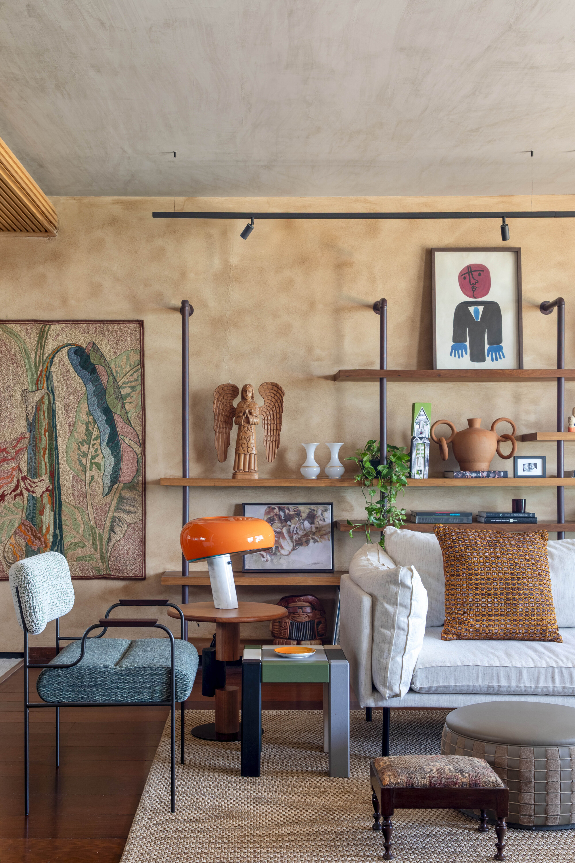 Living area with pipe-framed wooden shelves, a woven wall hanging and an orange mushroom lamp on a round side table