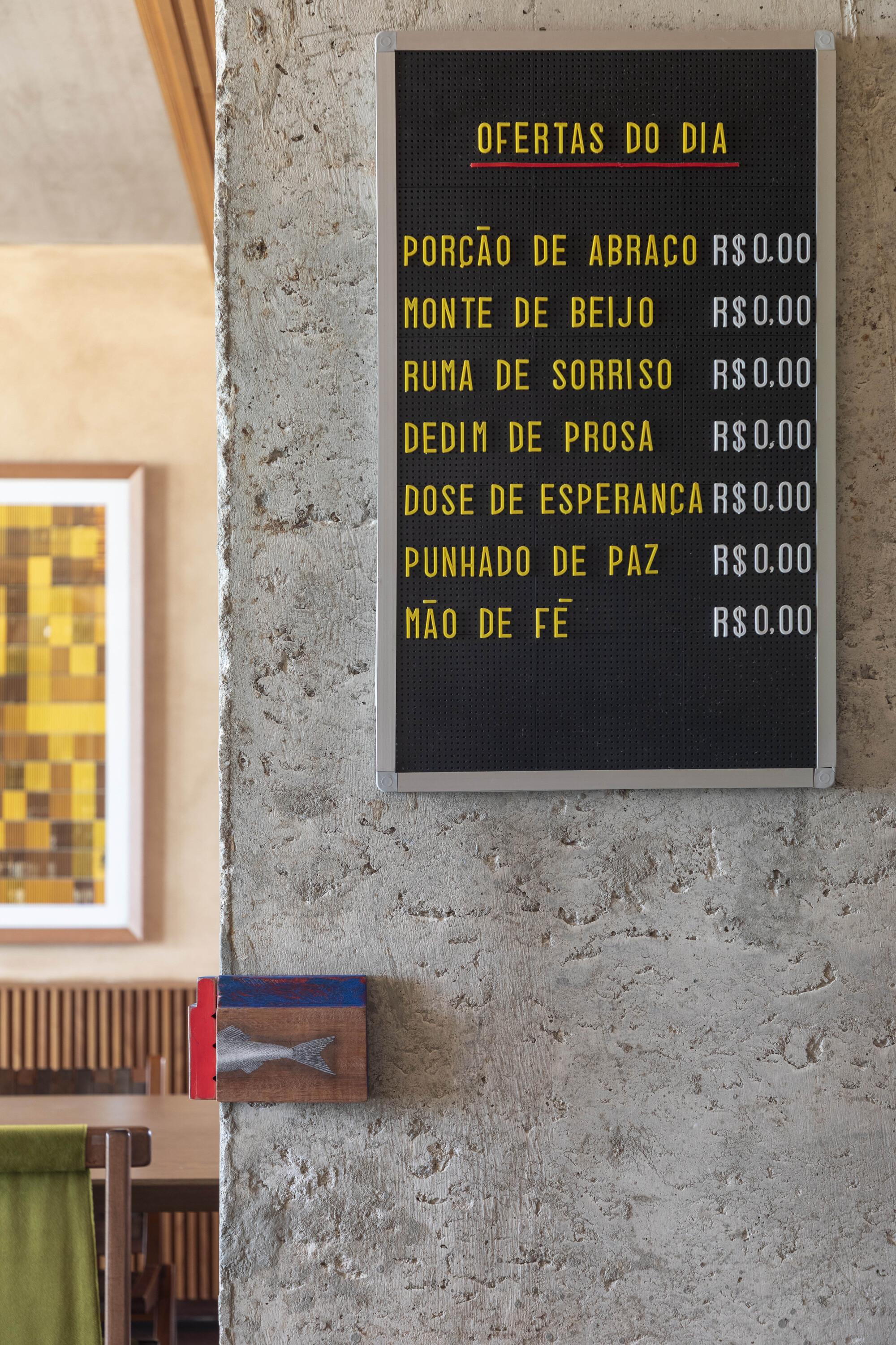 Black letter board listing daily offers beside a rough concrete column, with a small painted fish plaque below