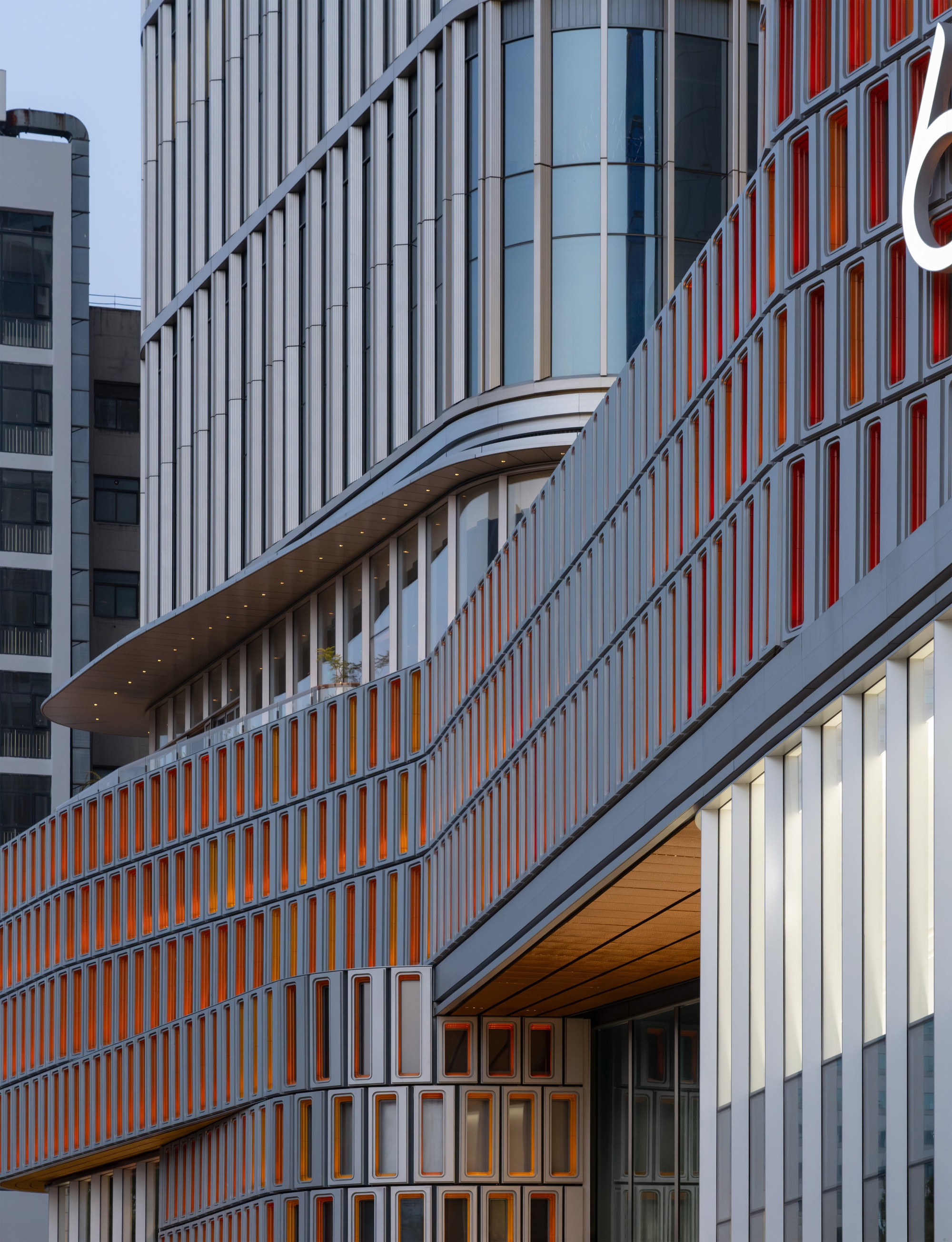 Close-up of curved facade bands with orange-lined window boxes above a timber-clad soffit and white fins