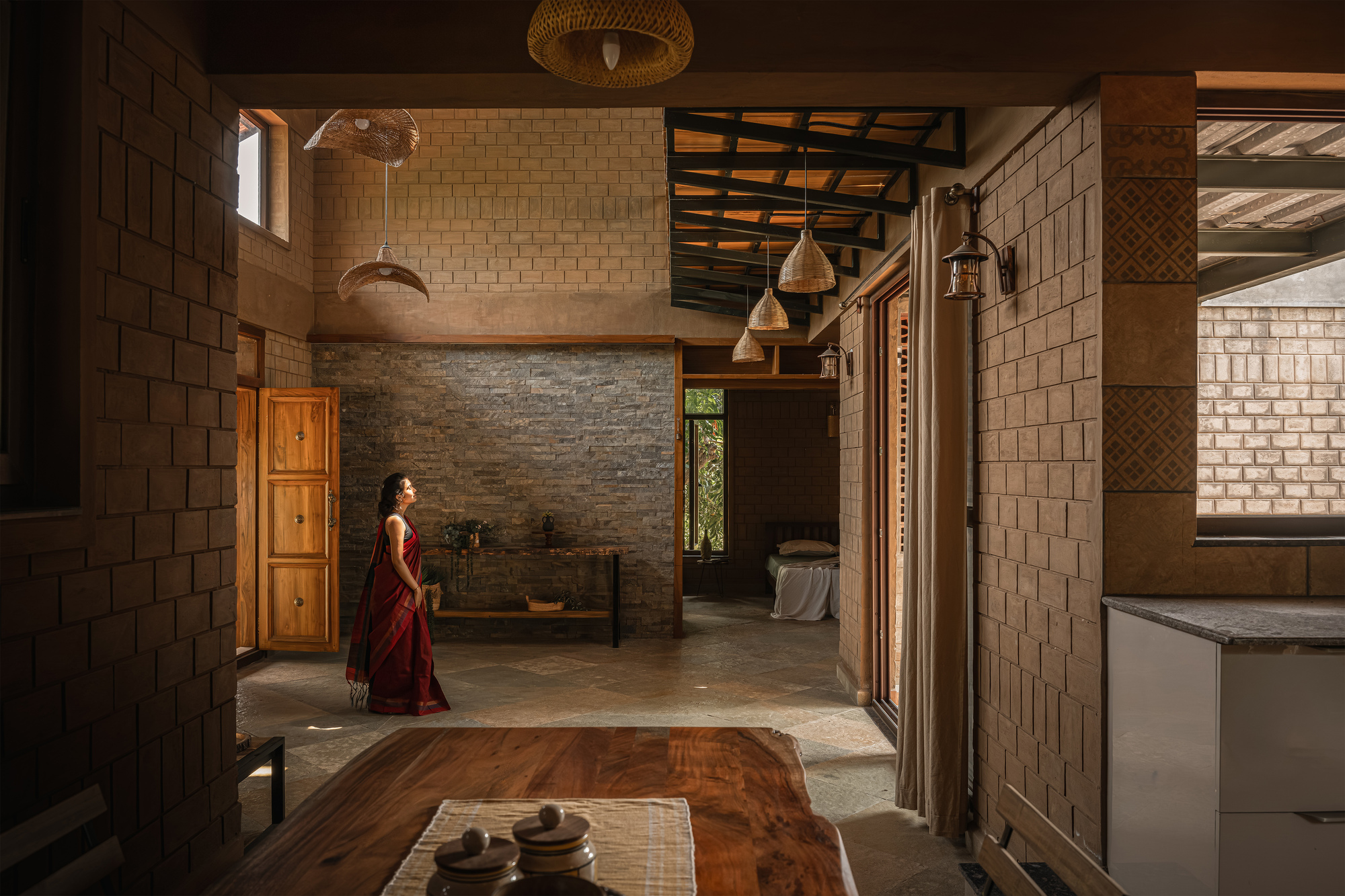 Interior view through a brick-walled dining area toward a stone feature wall, timber doors and a woman in a red sari