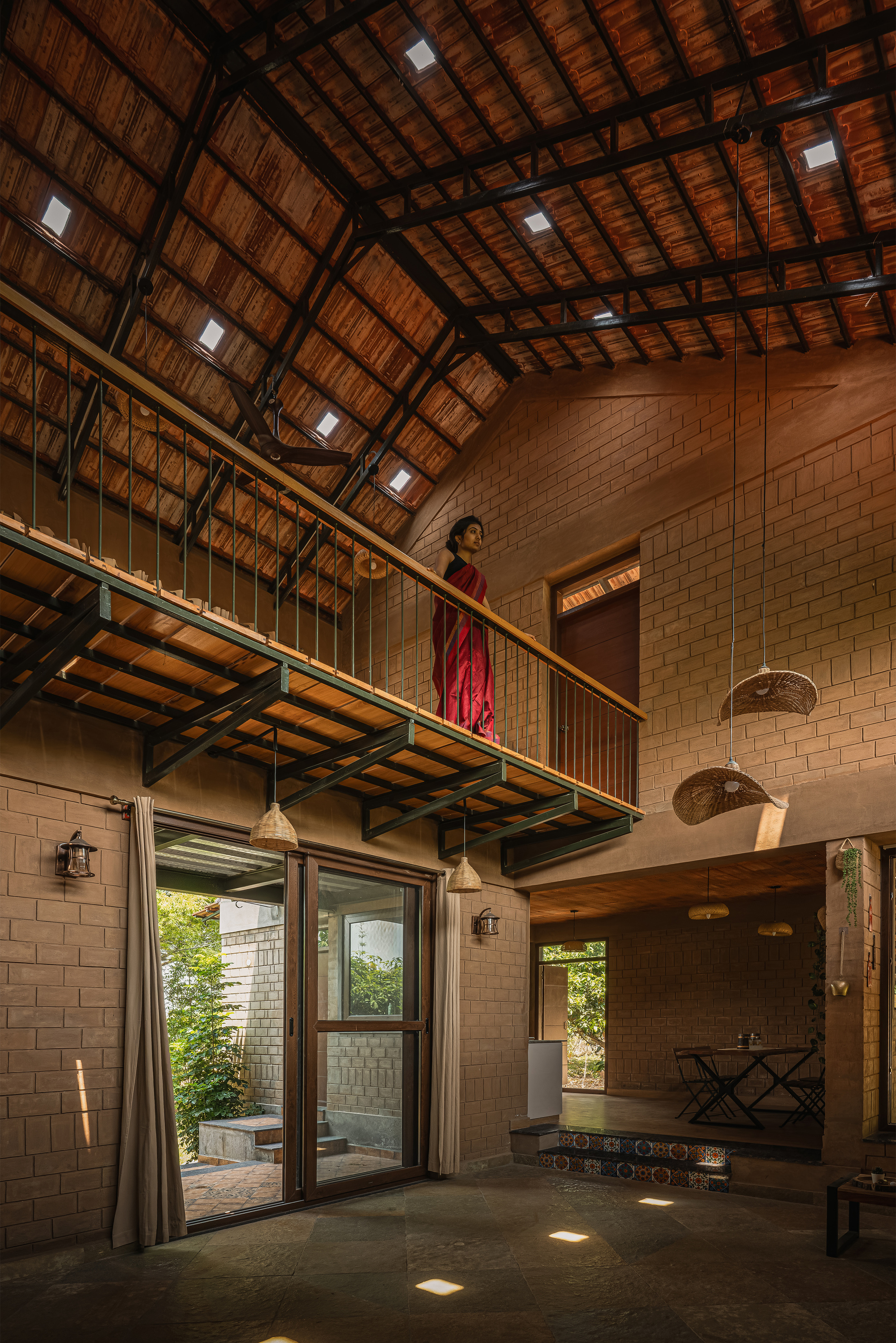 Interior with a steel-framed mezzanine walkway under a pitched tile roof with skylights, a woman in red standing at the railing
