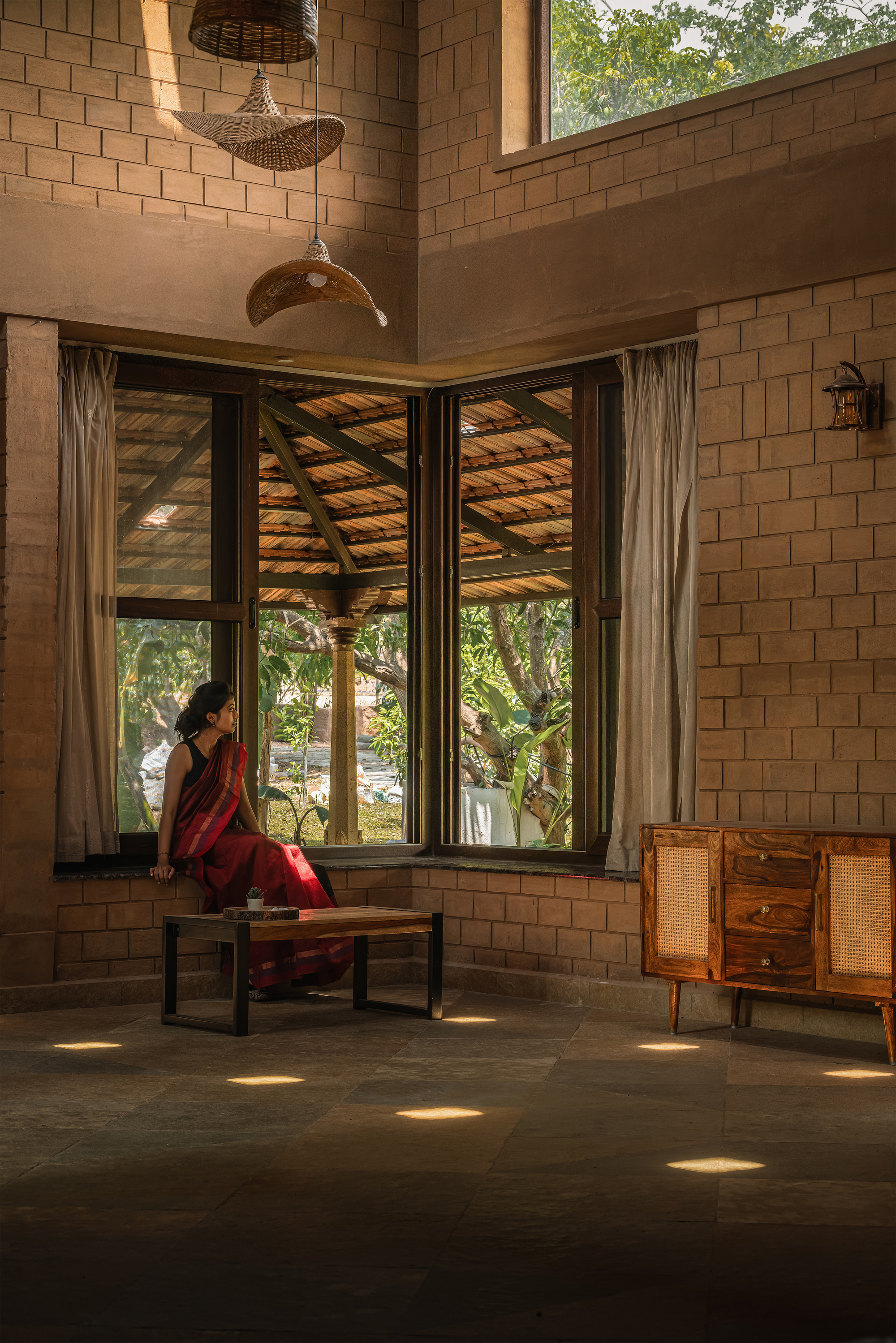 Corner window seat in a compressed earth block room, with a woman in a red sari and pools of sunlight on the stone floor
