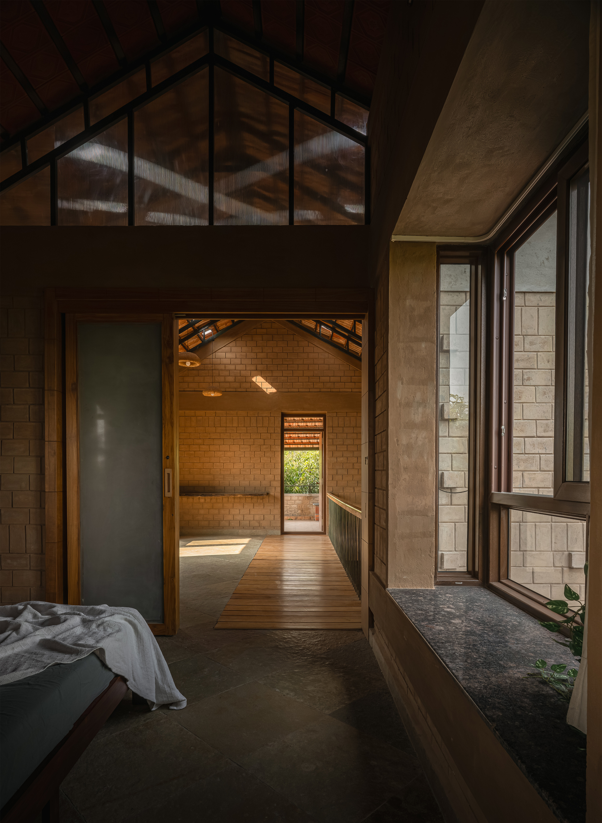 Upper-level bedroom opening through a sliding timber door to a bridge walkway, with a deep stone window sill in soft daylight