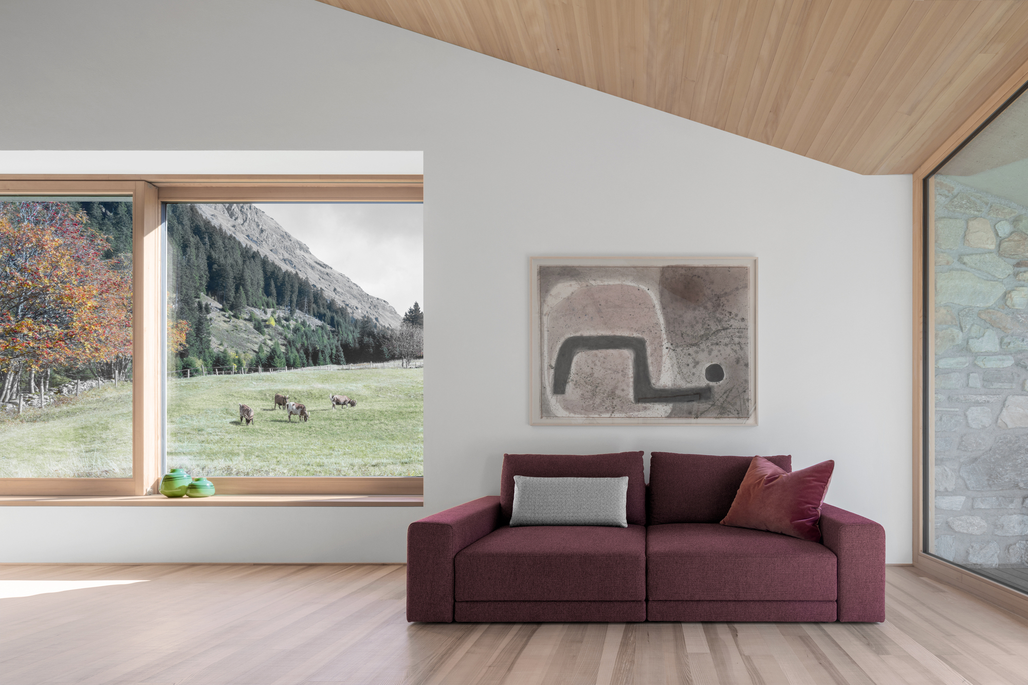 Burgundy sofa beneath a framed abstract print, with a timber-framed window looking onto grazing cows in an autumn meadow
