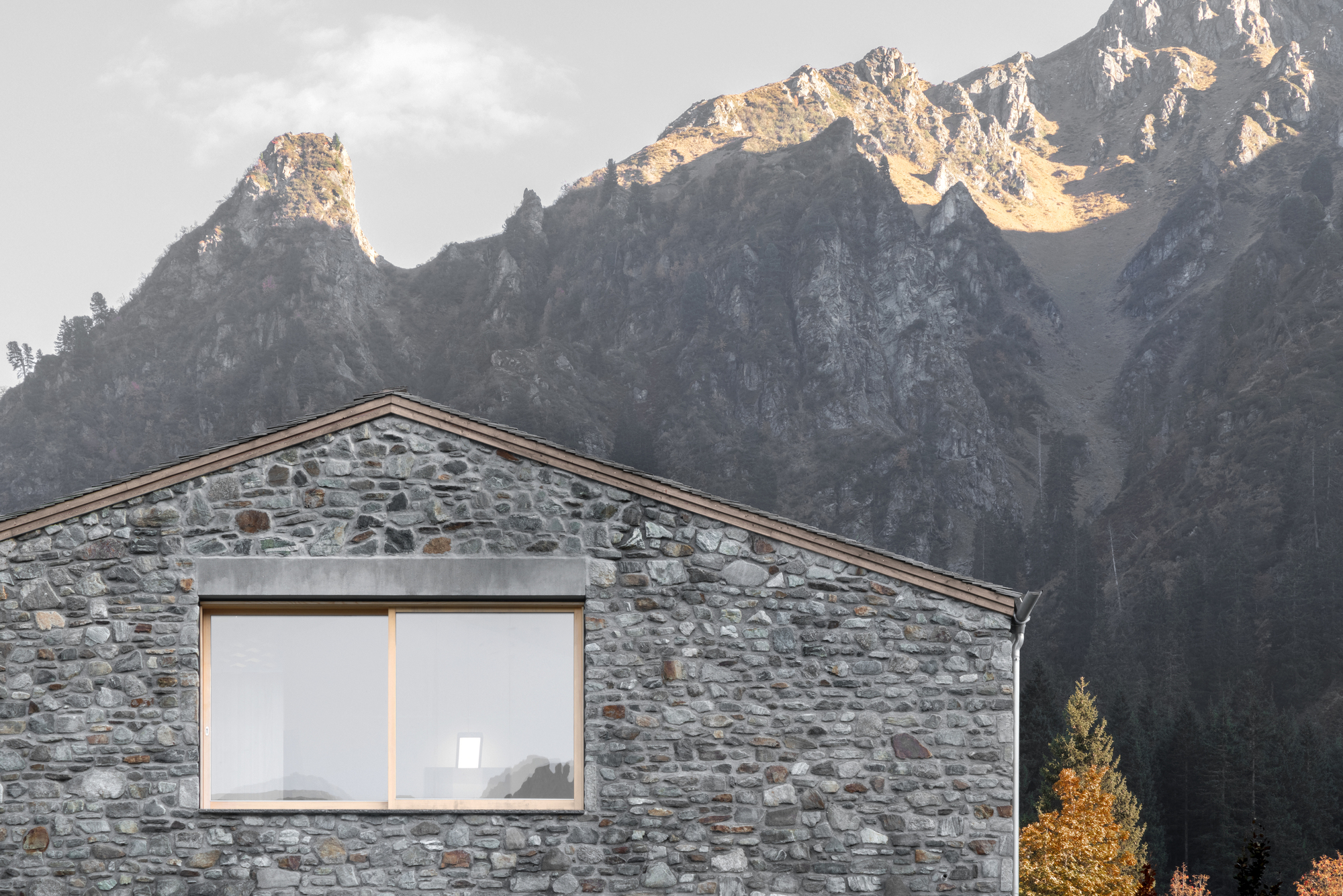 Close-up of the stone gable with a wood-framed window against a rocky peak in late light