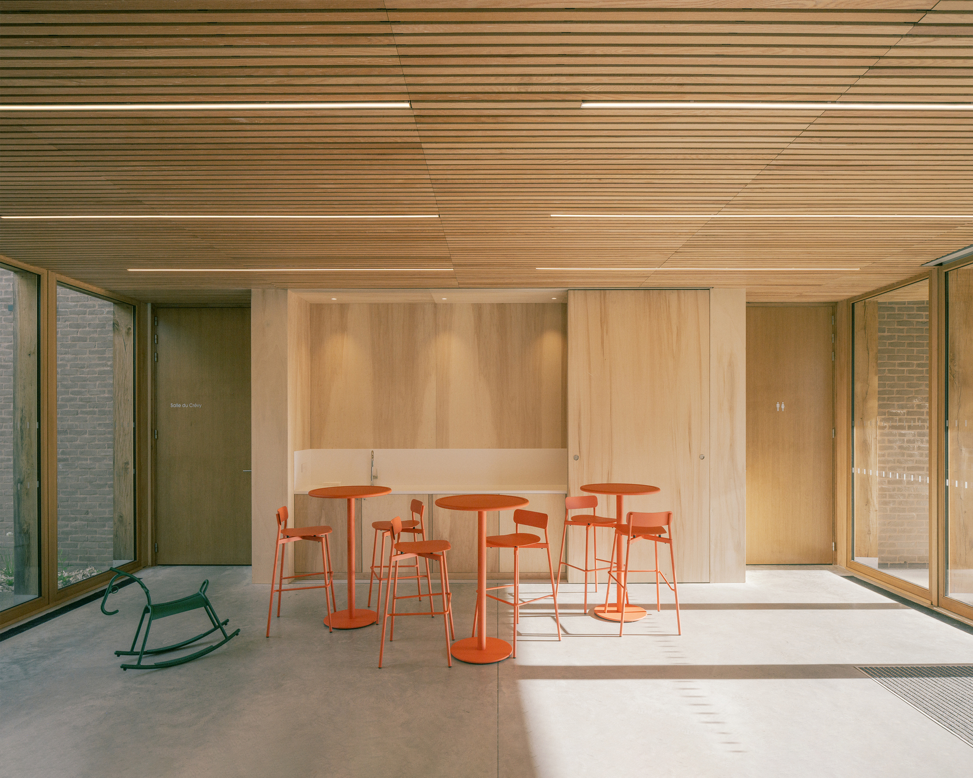Interior hall with orange bar tables and stools, a green rocking horse and a timber slat ceiling lit by sunlight patches