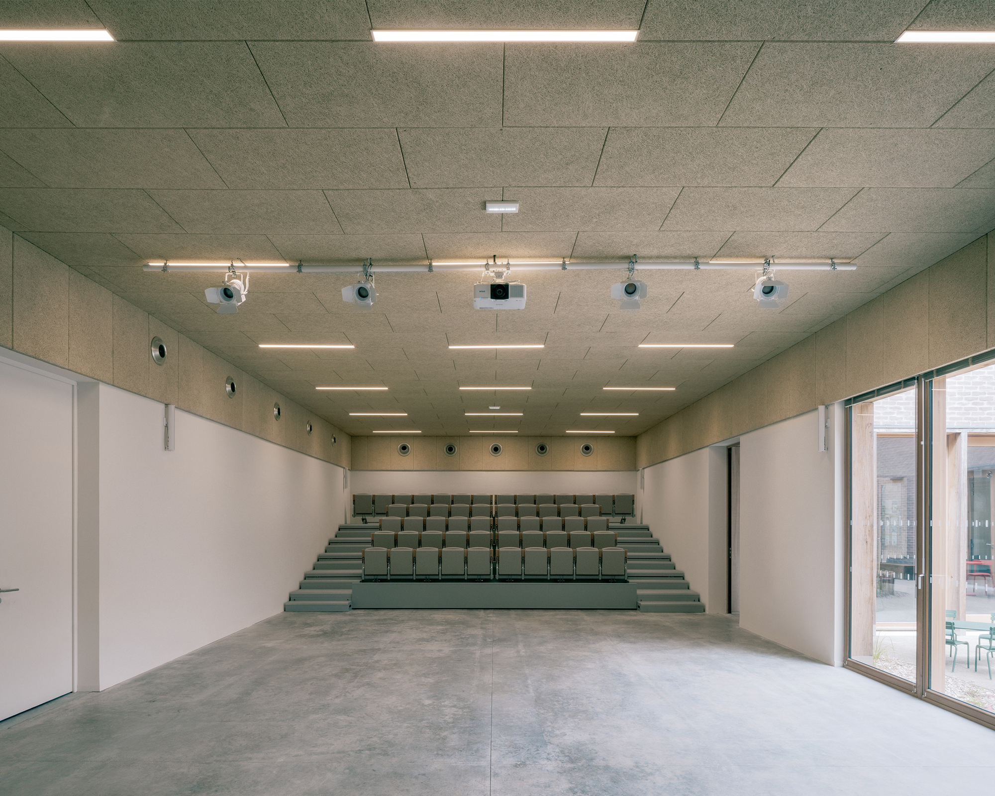 Meeting room with raked tiered seating at the far end, projectors on a ceiling rail and a glazed door onto a courtyard