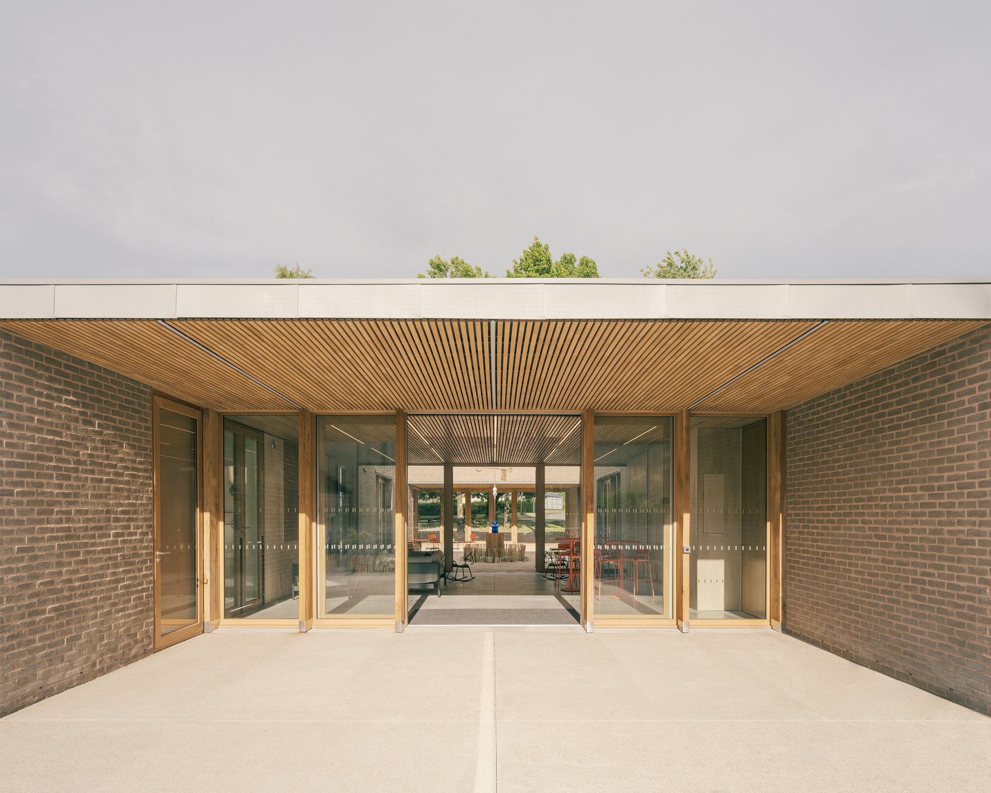 Entrance opening between two brick walls, with a timber slat soffit and glazed timber frames looking through to the courtyard beyond