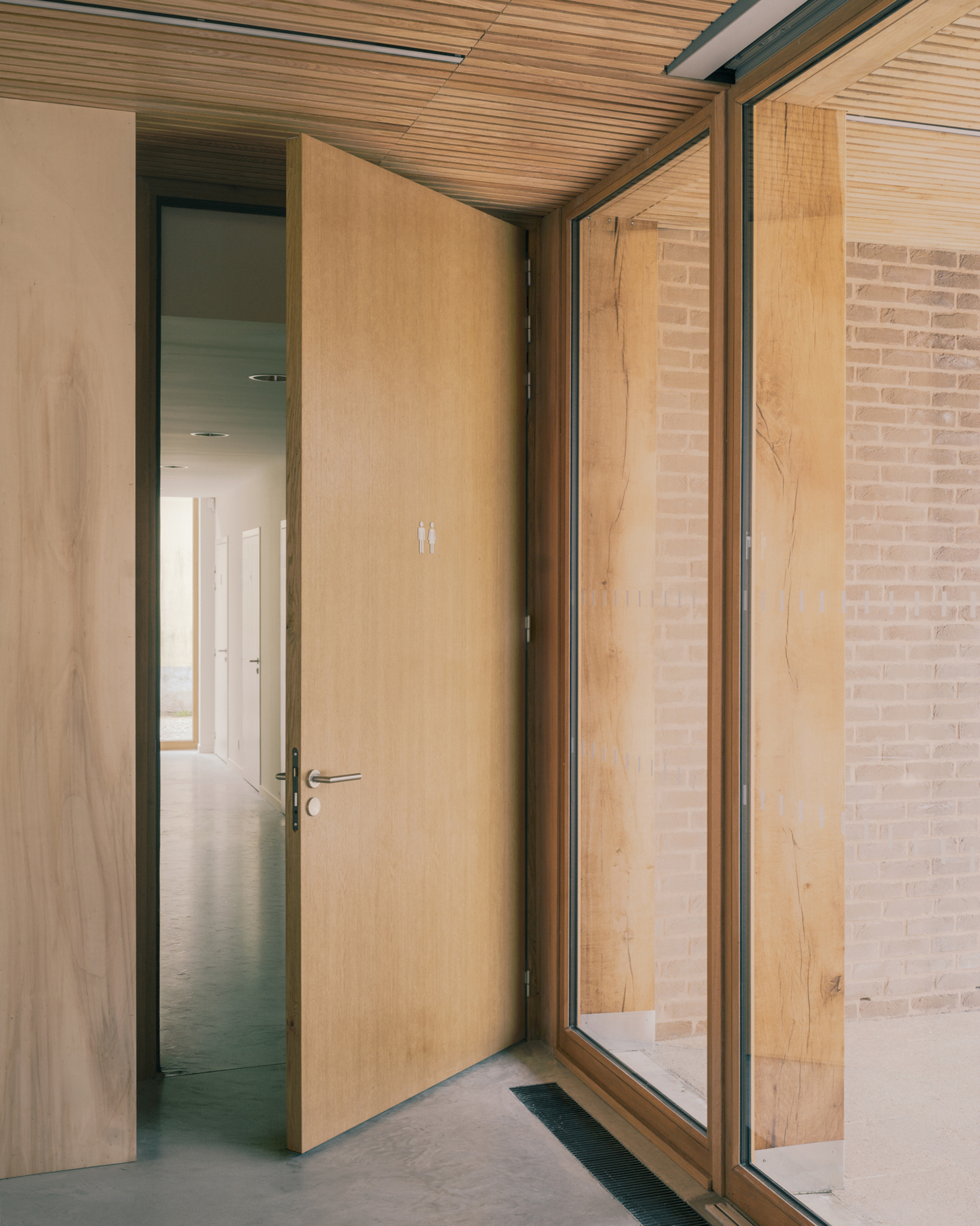 Oak pivot door standing open beside a glazed corner with oak posts and a pale brick wall outside