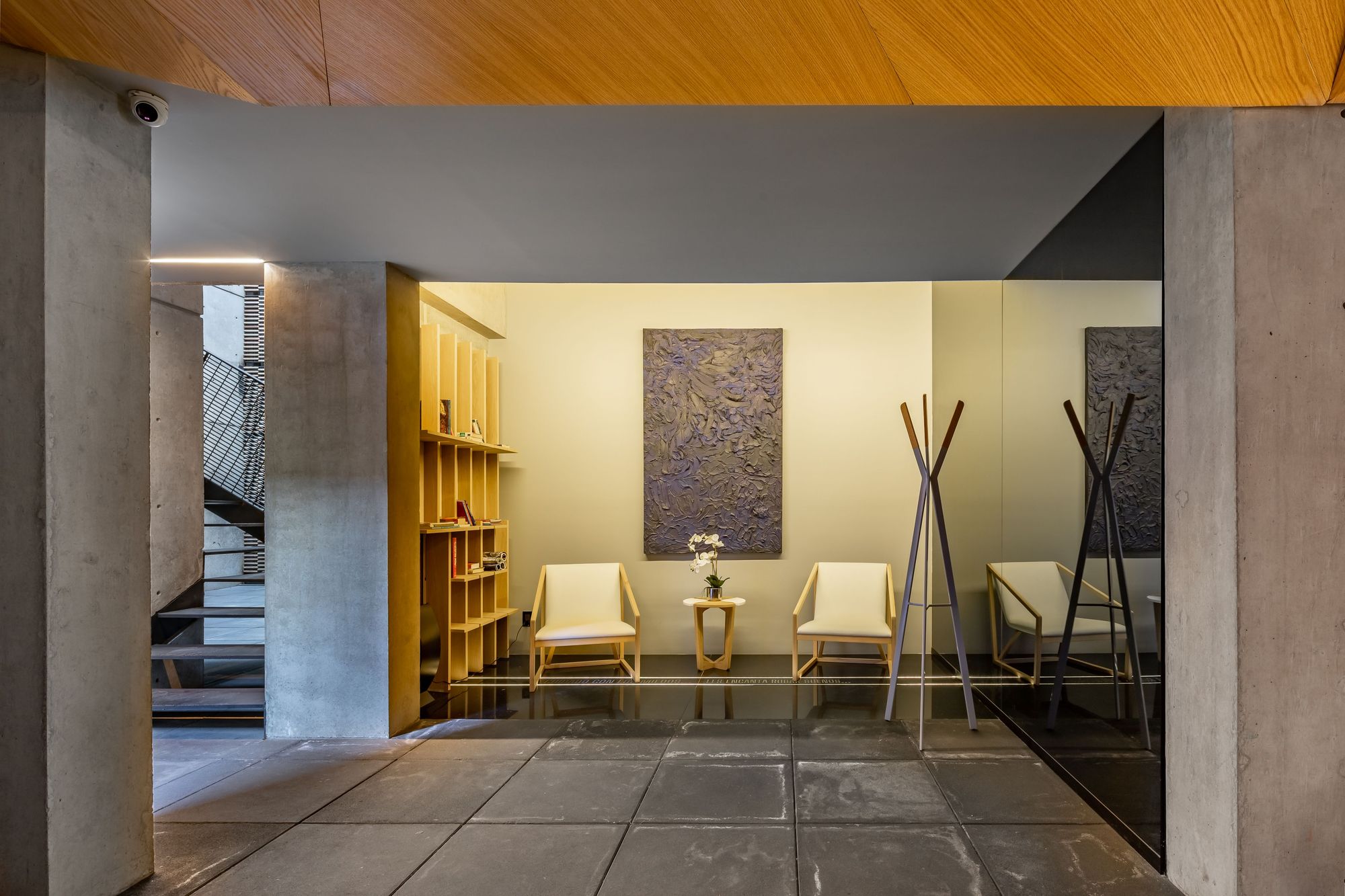 Lobby seating area with two cream chairs, a coat stand and a textured wall panel between board-formed concrete columns