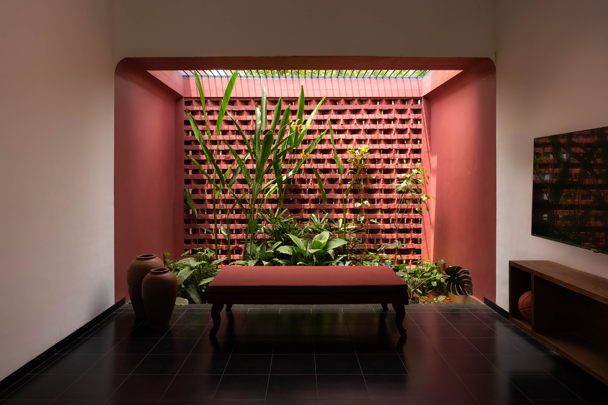 Sitting room opening onto a planted light well with a red brick lattice wall, a low bench and clay pots on black floor