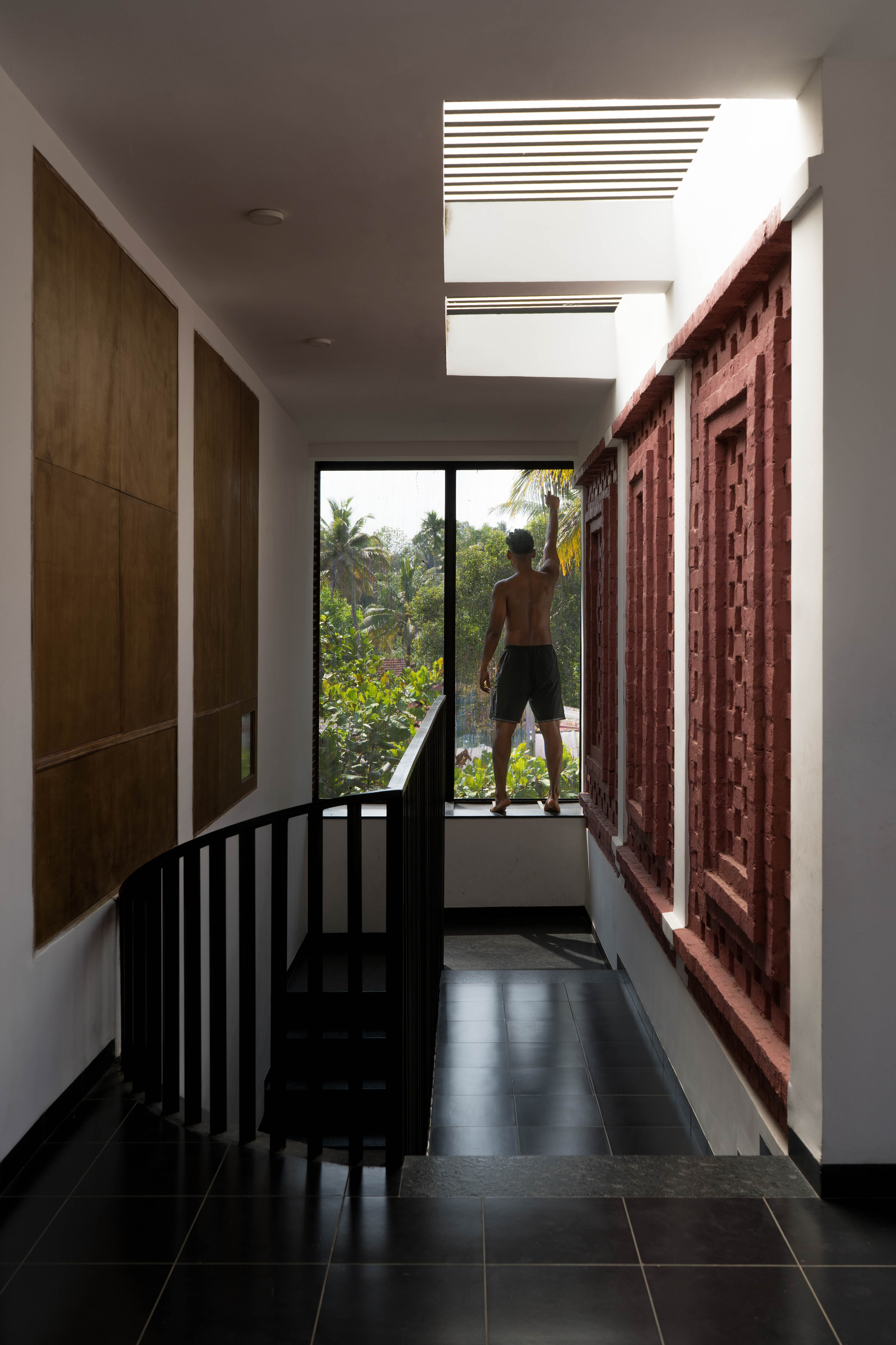 Upper landing with a red brick lattice screen and a man at the window facing palm trees in daylight