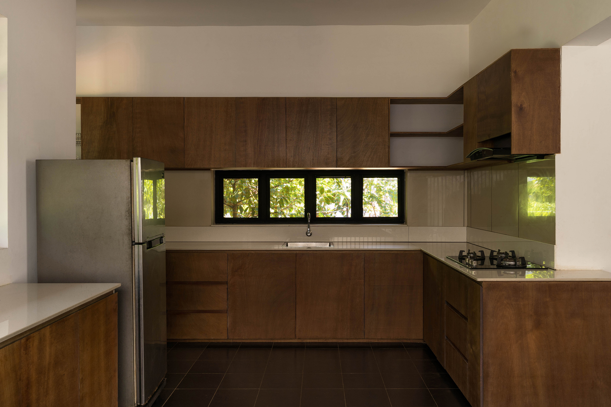 U-shaped timber kitchen with a steel refrigerator and a strip window framing green foliage in daylight