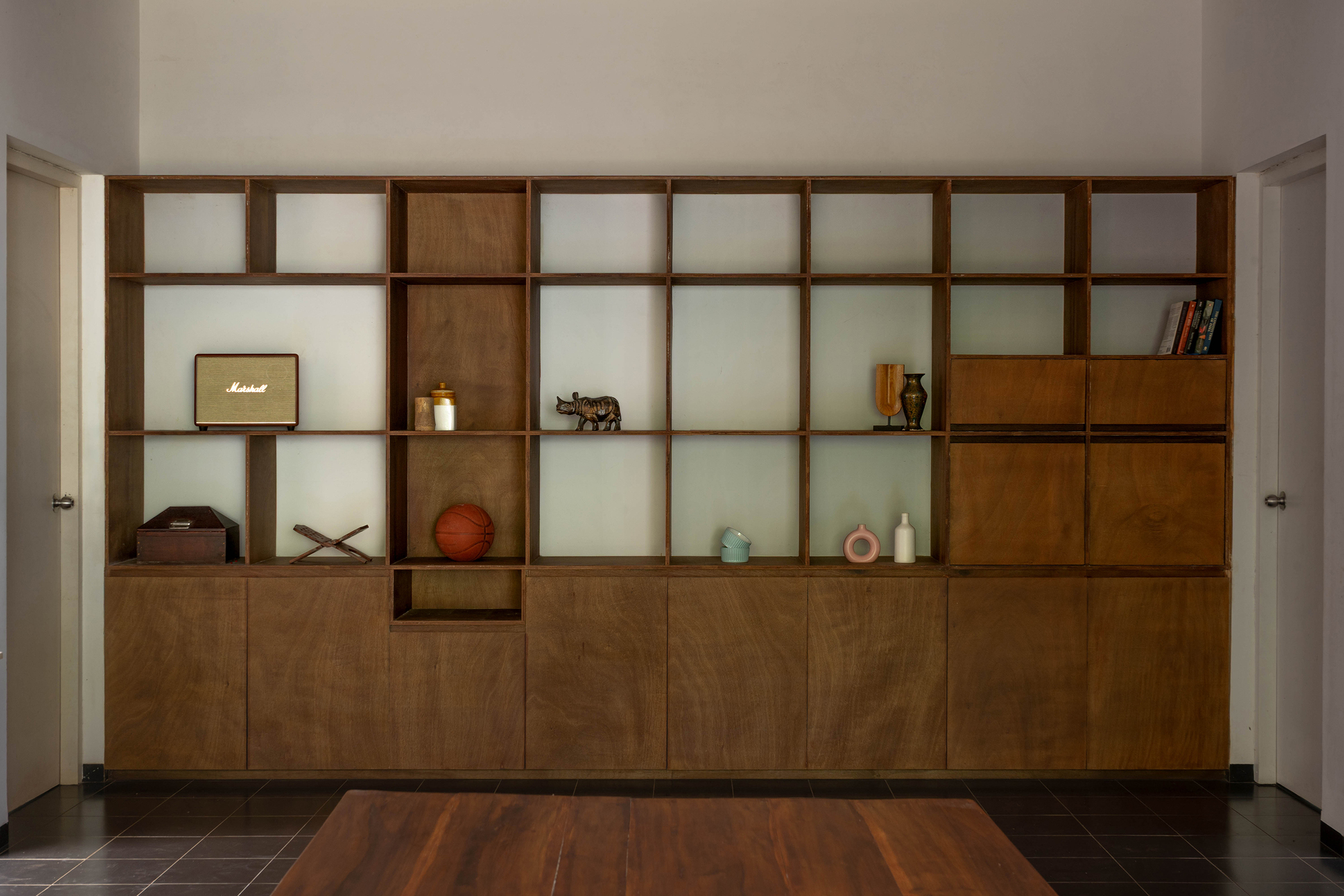 Timber shelving wall with open cubbies and lower cabinets holding books, a speaker and a basketball above a wooden table