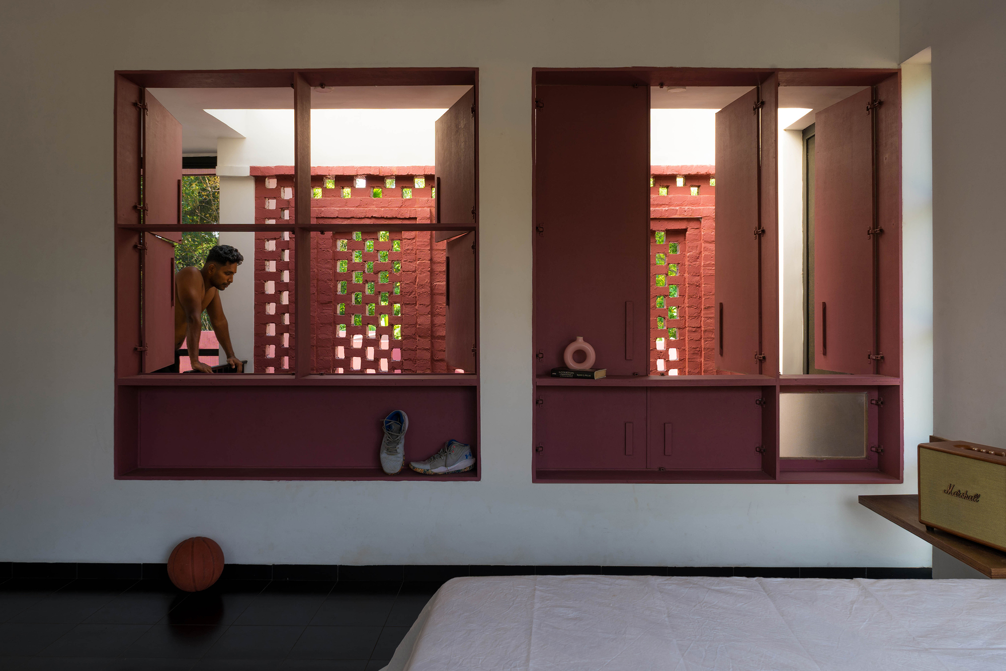 Two recessed maroon window cabinets framing a perforated red brick screen, with a man leaning outside in daylight