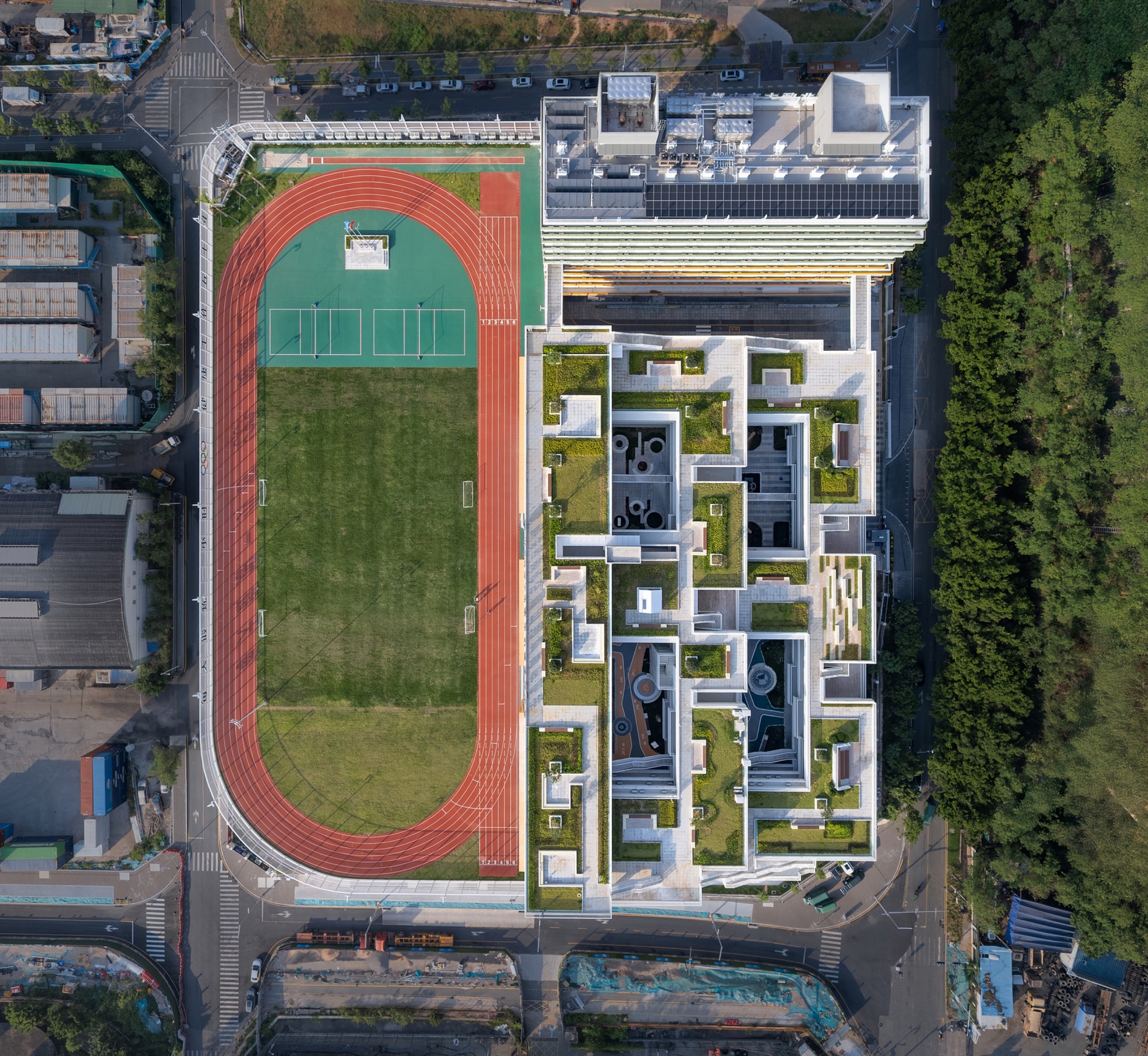 Aerial top-down view of the running track and sports field beside a terraced building with planted roof courtyards
