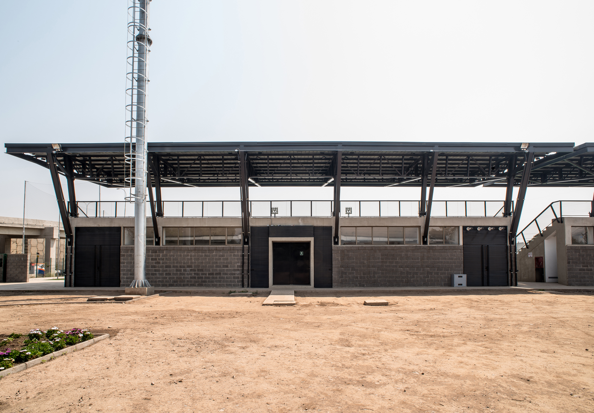 Rear elevation of the grandstand base with concrete block walls, black doors and slanted steel struts under a hazy sky